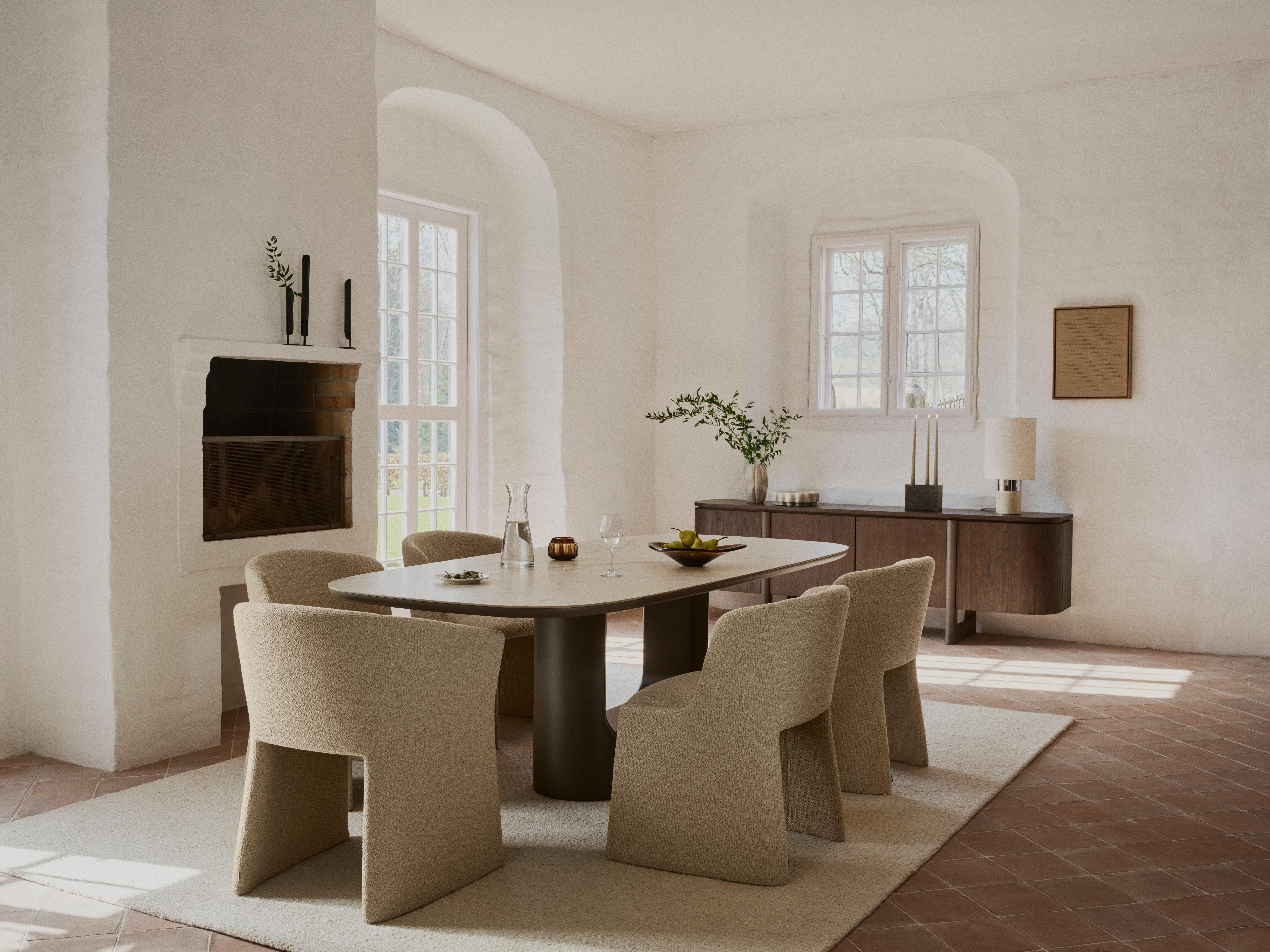 Modern dining table with six upholstered chairs, set with glassware and fruit bowl.