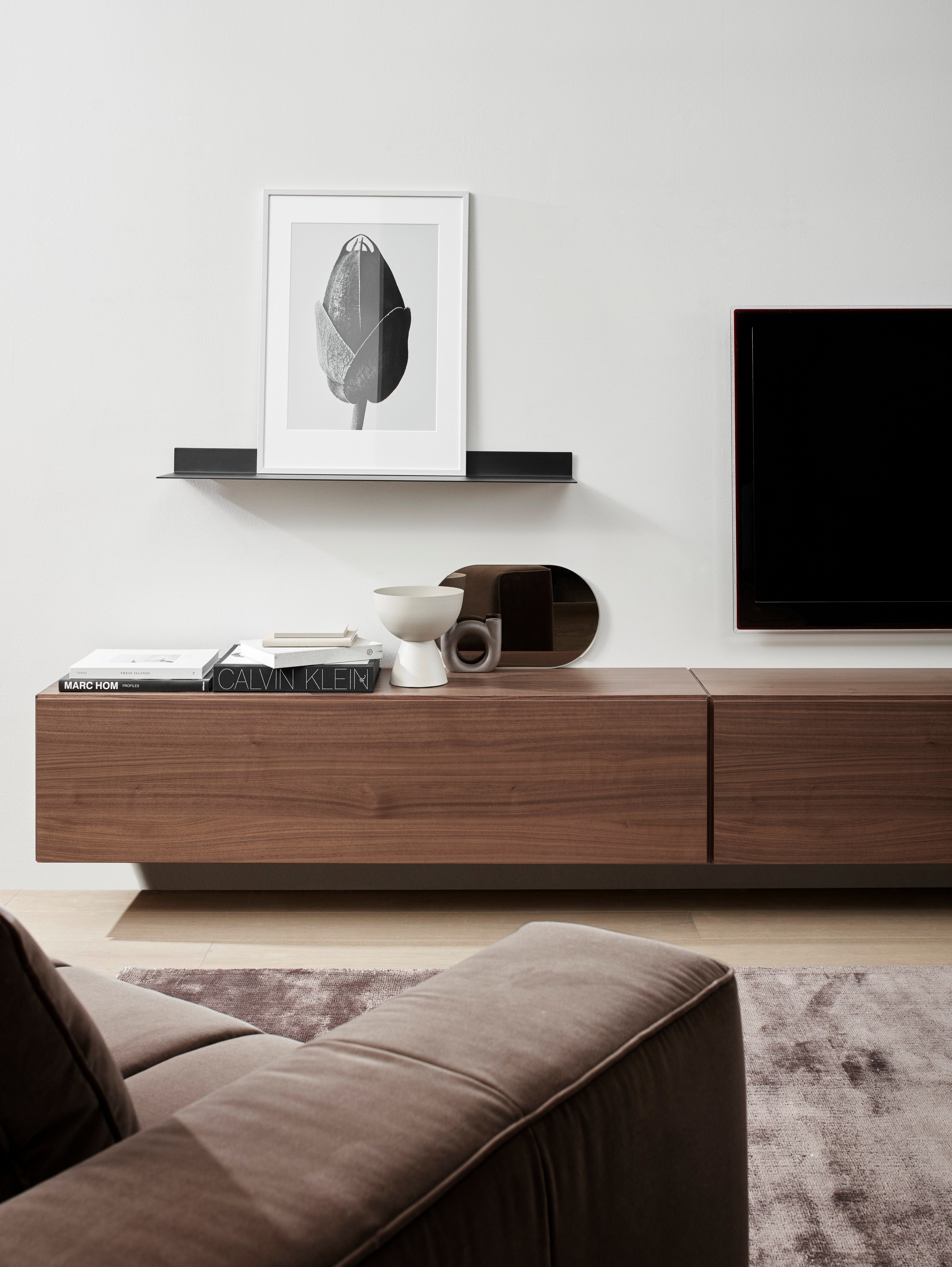 Minimalistinen olohuoneen yksityiskohta, jossa on ruskea sohva, puinen mediayksikkö, abstraktia taidetta ja moderneja sisustustuotteita.