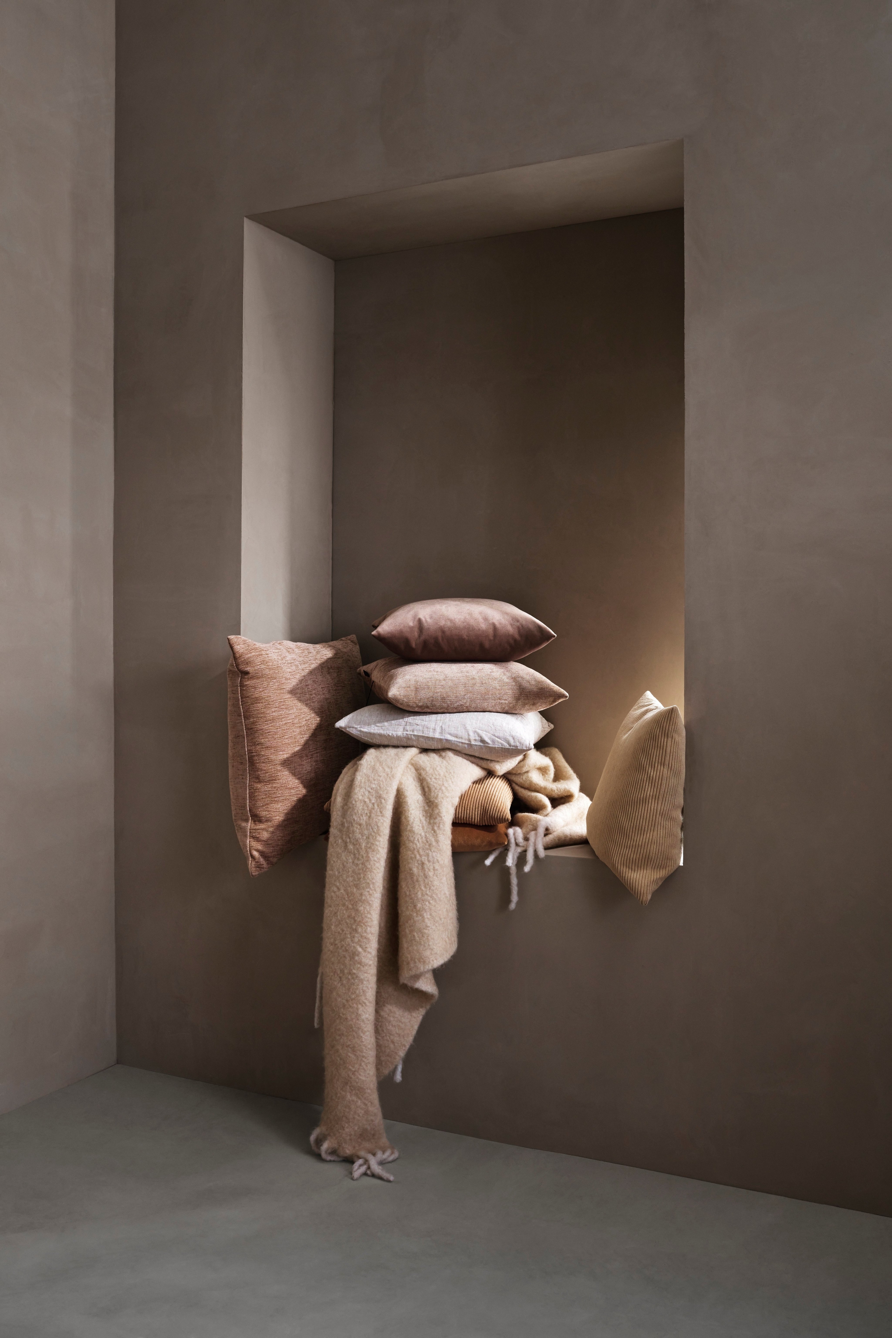 A cozy nook with piled cushions and a blanket in shades of beige and brown.