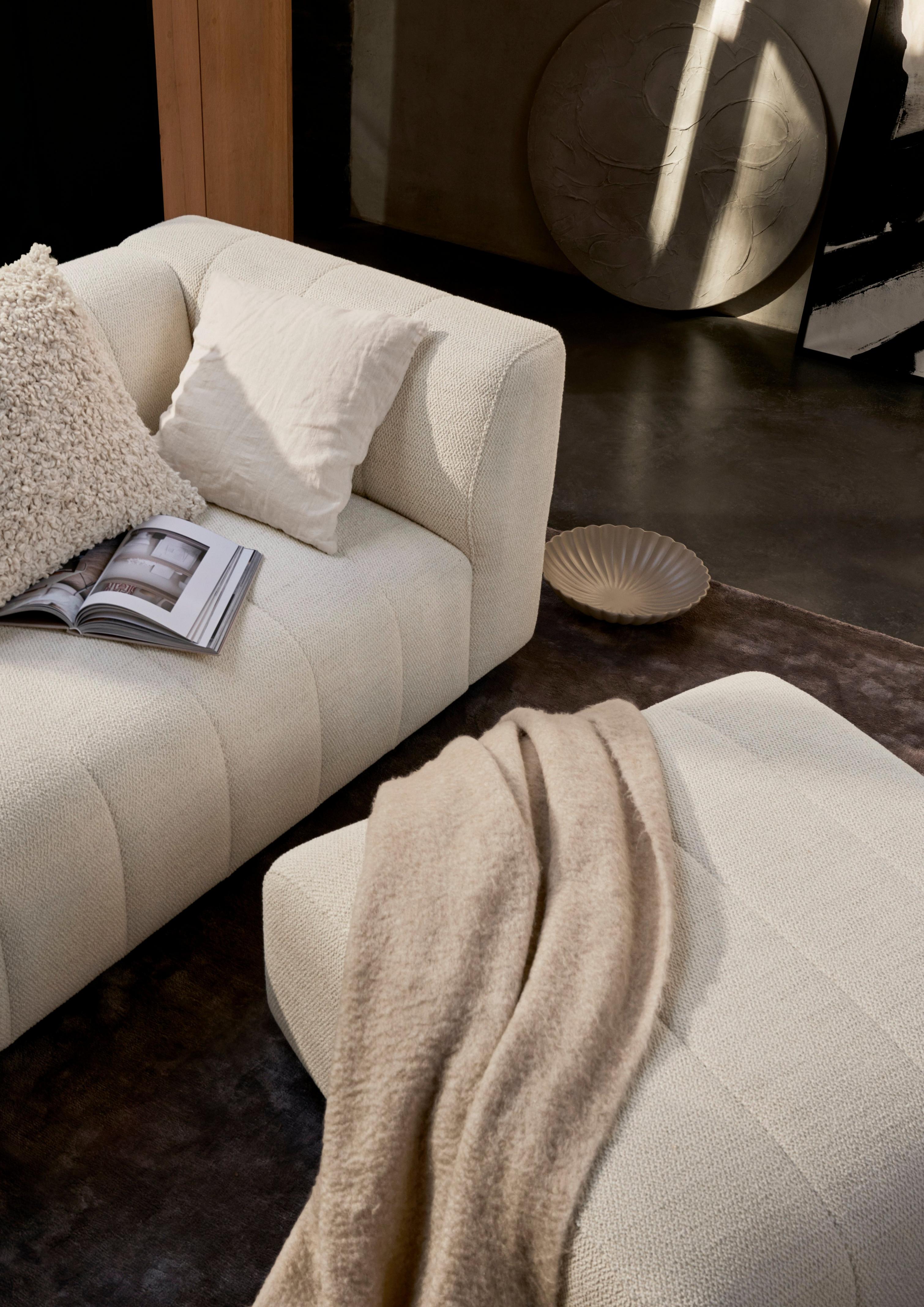 Canapé beige avec coussins blancs et livre ouvert, couverture beige sur le côté.