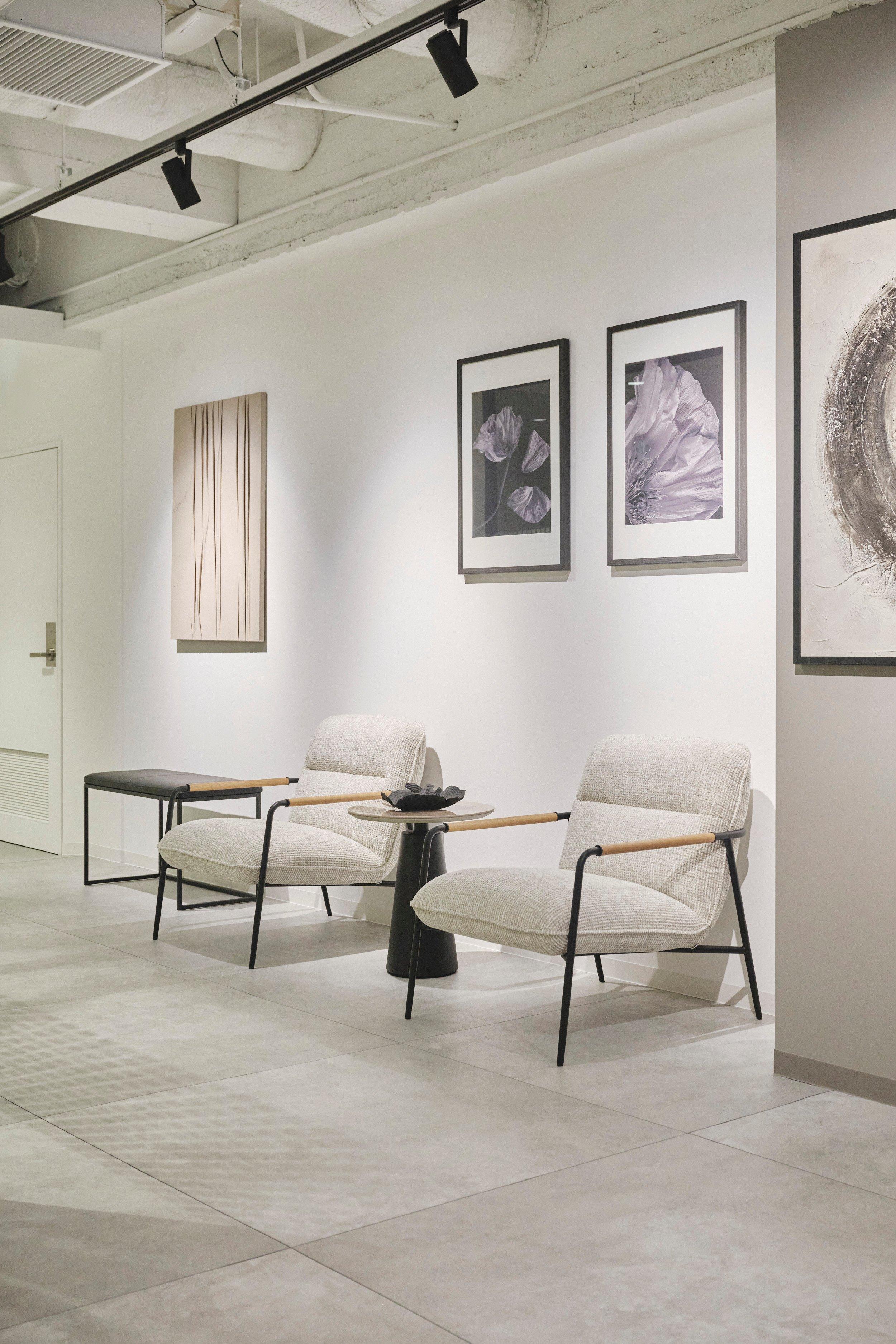 Dos sillones beige con mesa pequeña, arte abstracto en la pared. Decoración moderna y minimalista.