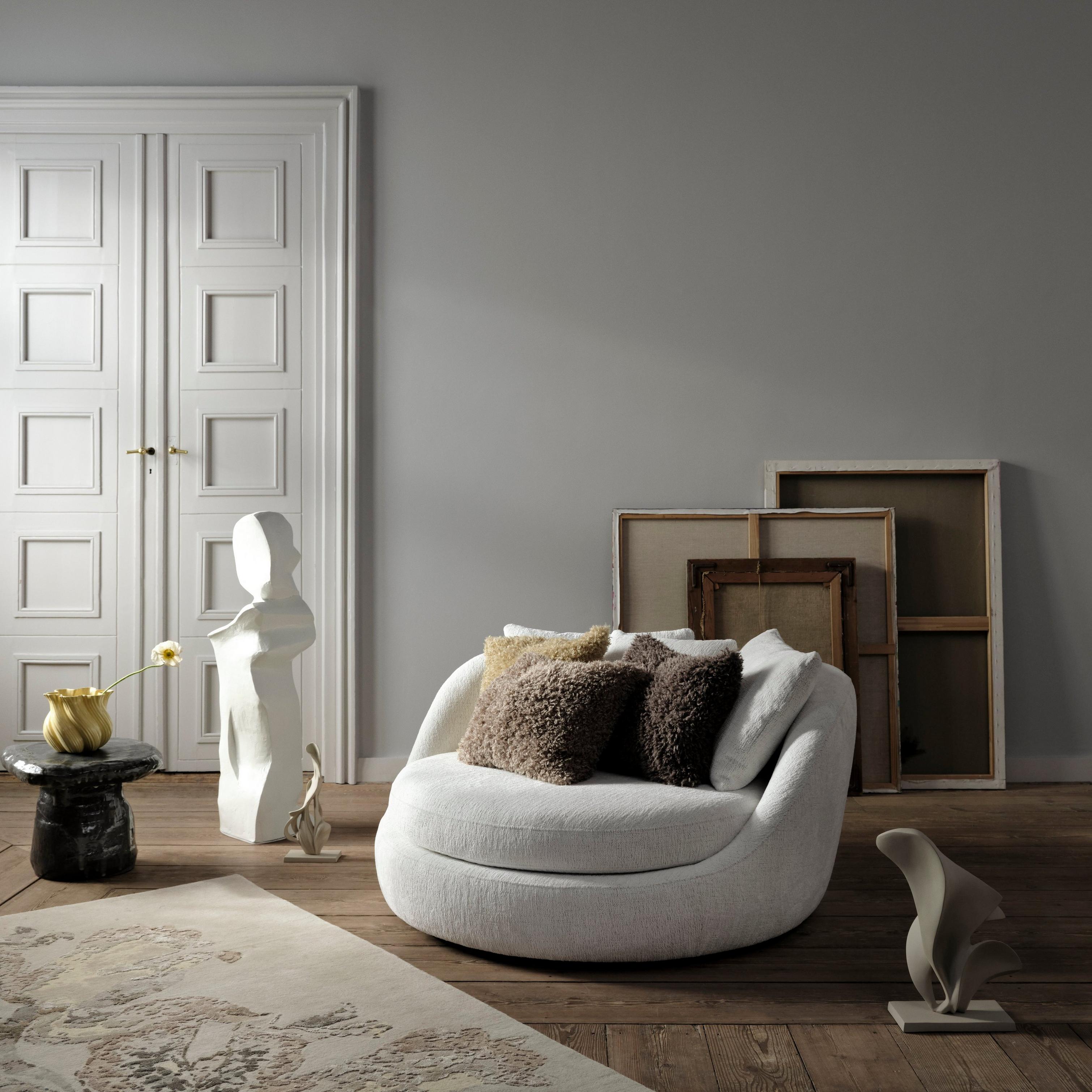 Modern living room with a white armchair, abstract sculptures, and framed canvases.
