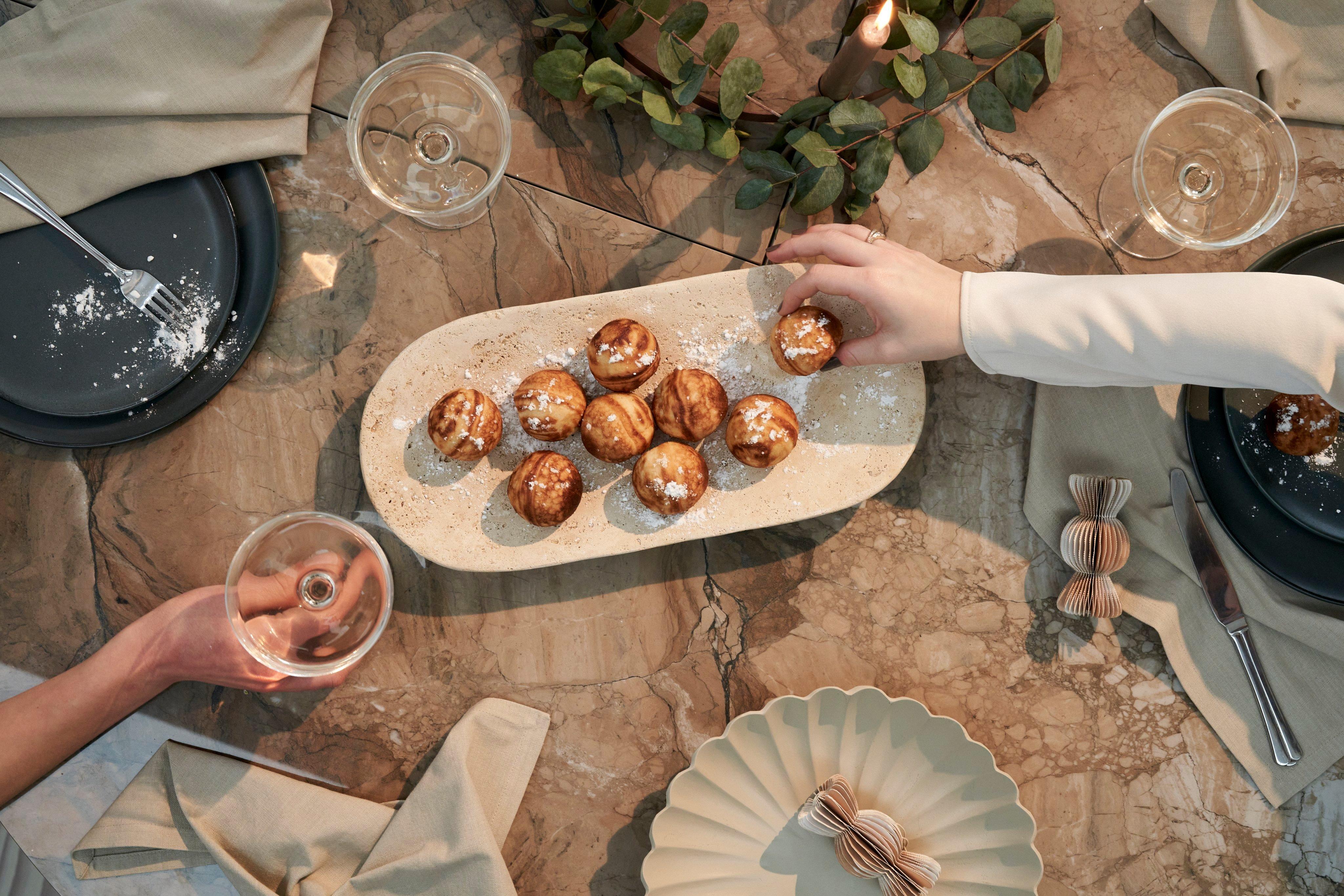 ナプキン、皿、グラスを並べてセッティングしたセラミックのテーブルの上に楕円形の皿が置かれ、その上に粉砂糖を振りかけた丸いケーキがのっている。