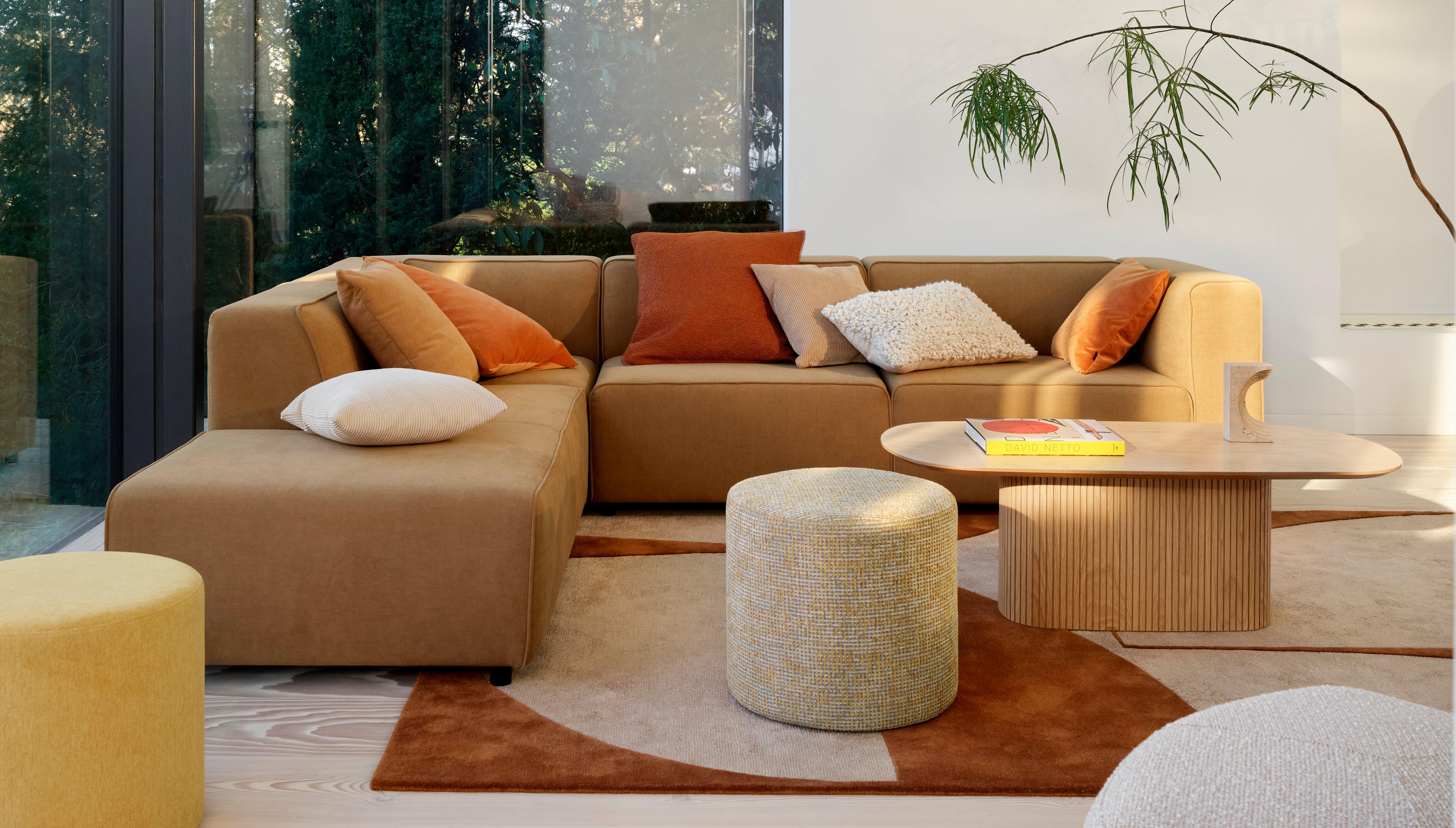 Acogedora sala con sofá modular, varios cojines, pufs Eden redondos, mesa de centro Santiago, grandes ventanales y vistas a los árboles.