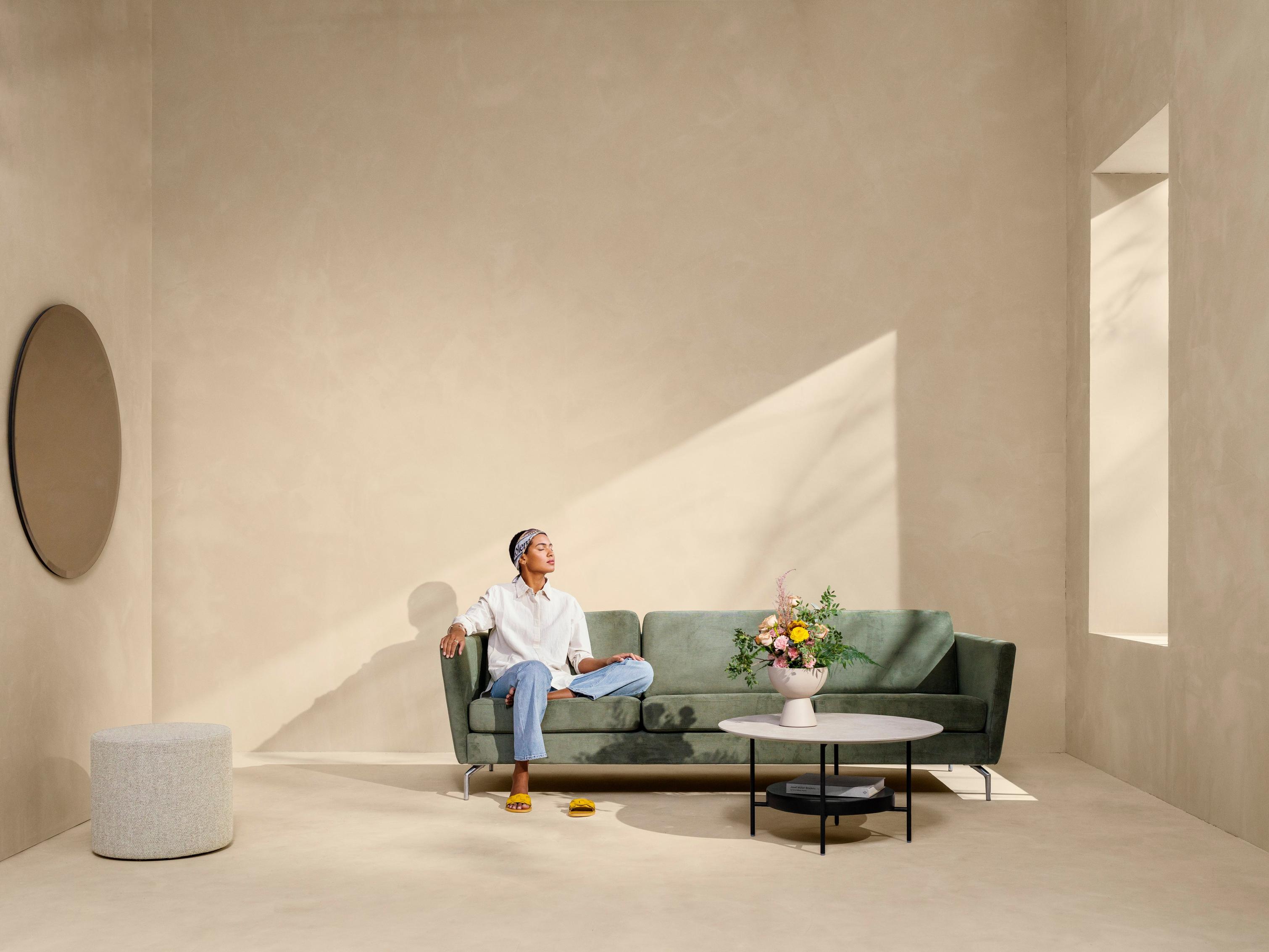 Woman sitting on the Osaka sofa in green Skagen fabric.