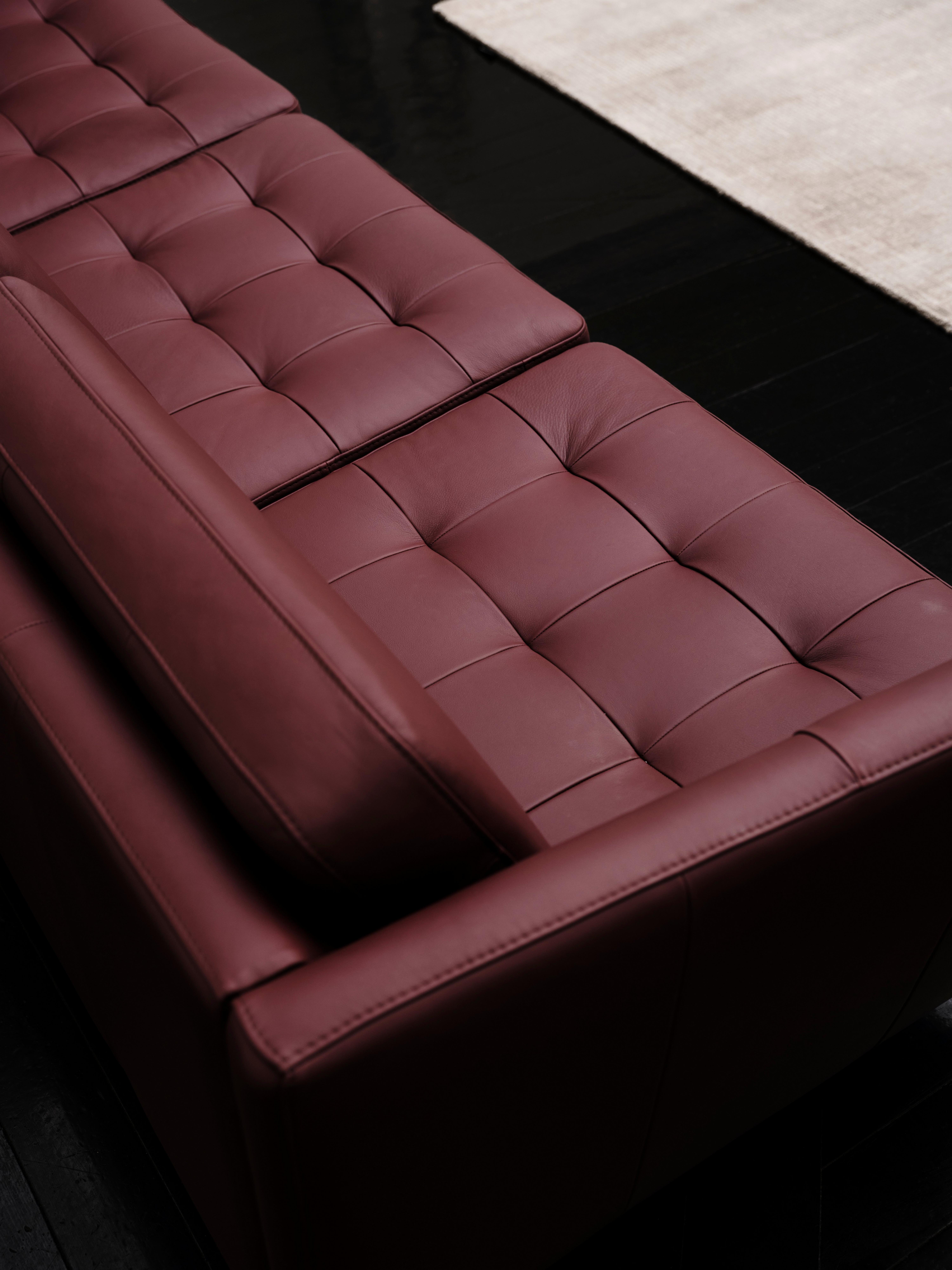 Bordeauxfarbenes Ledersofa mit Knopfheftung auf dunklem Boden und hellem Teppich.