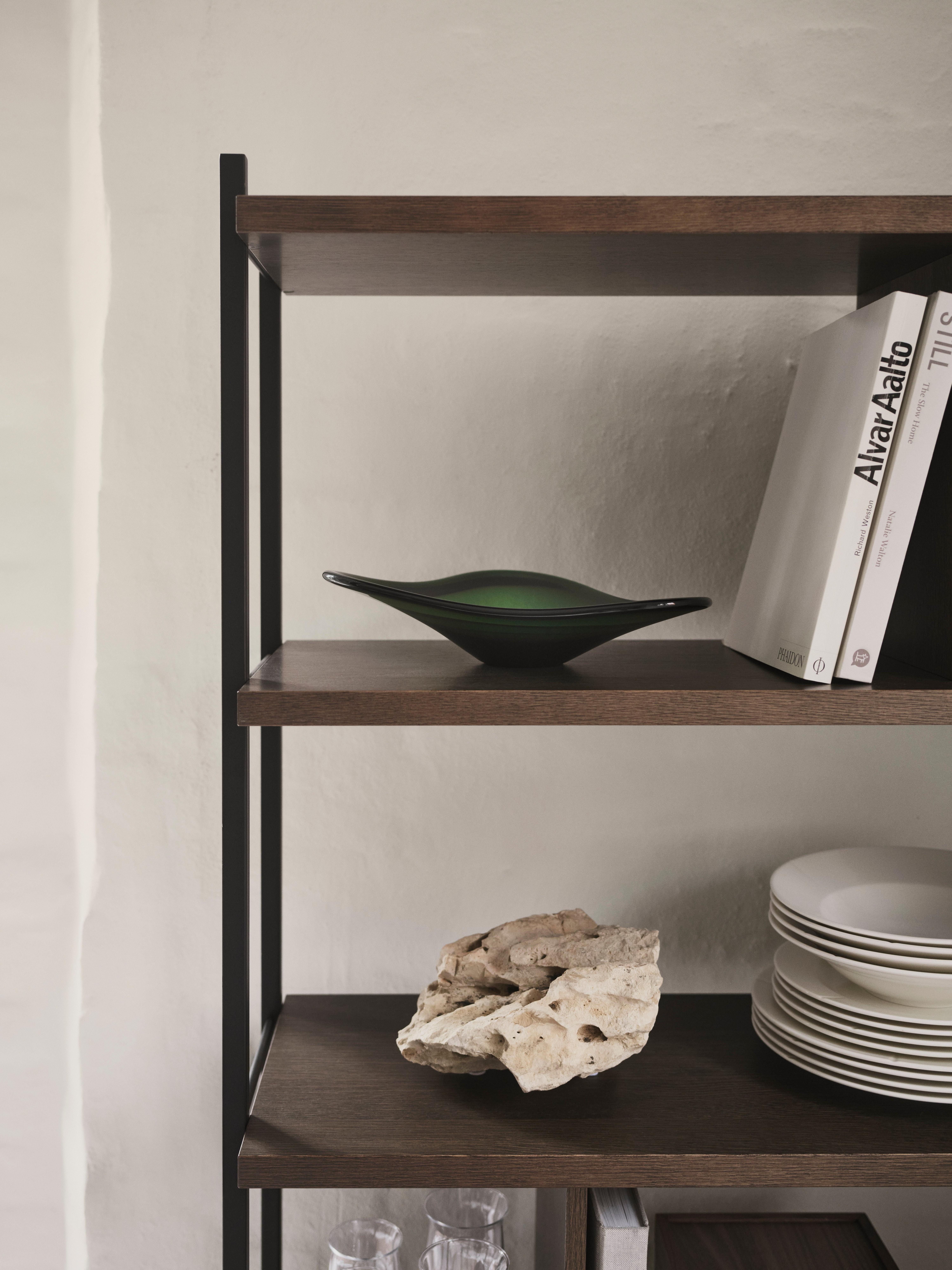Wood and metal shelving unit with a green glass bowl, books, stacked plates and a rock.