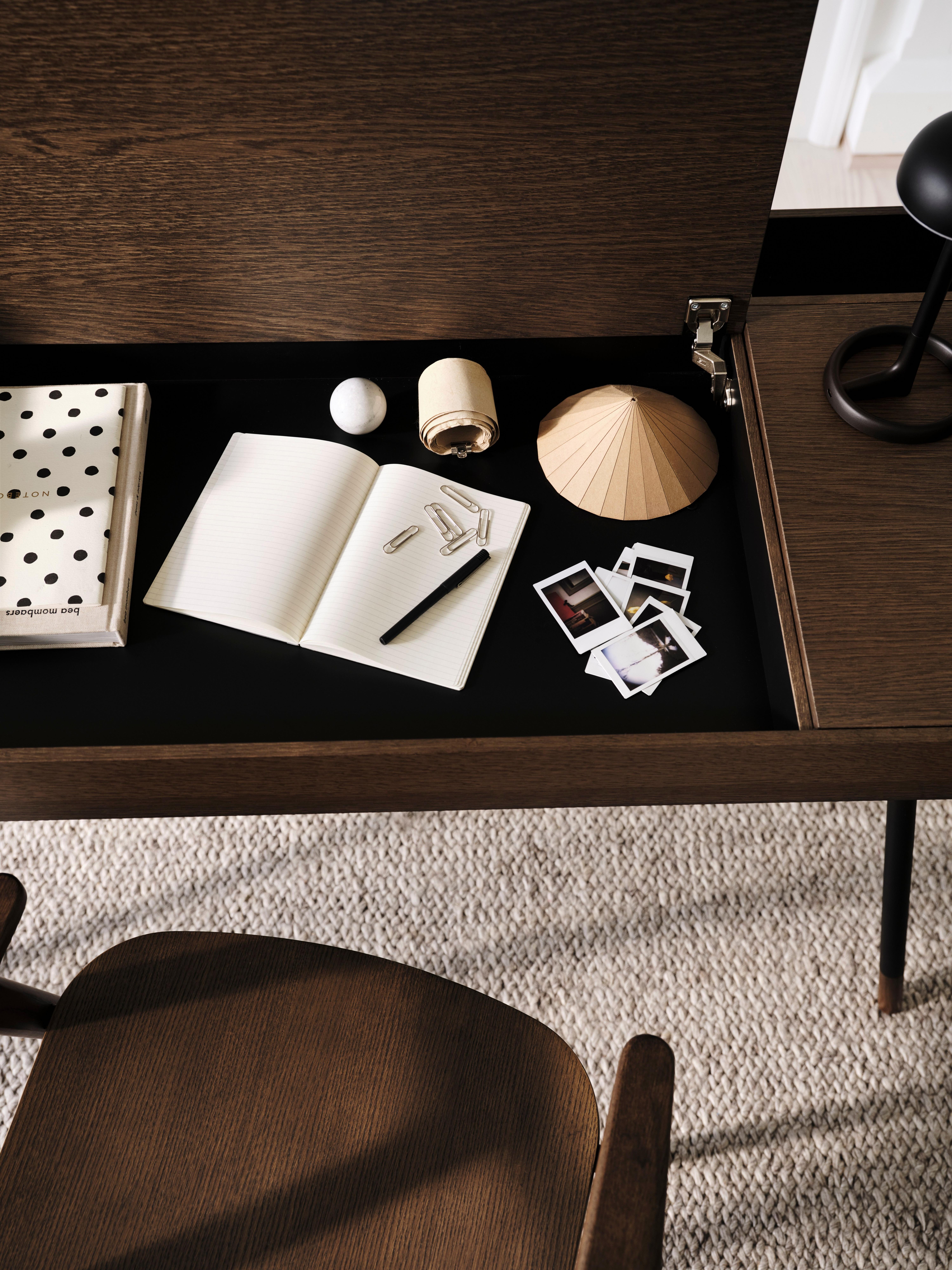 Carnet à pois, cahier ouvert, stylo, trombones, photos et objets décoratifs sur un bureau en bois.