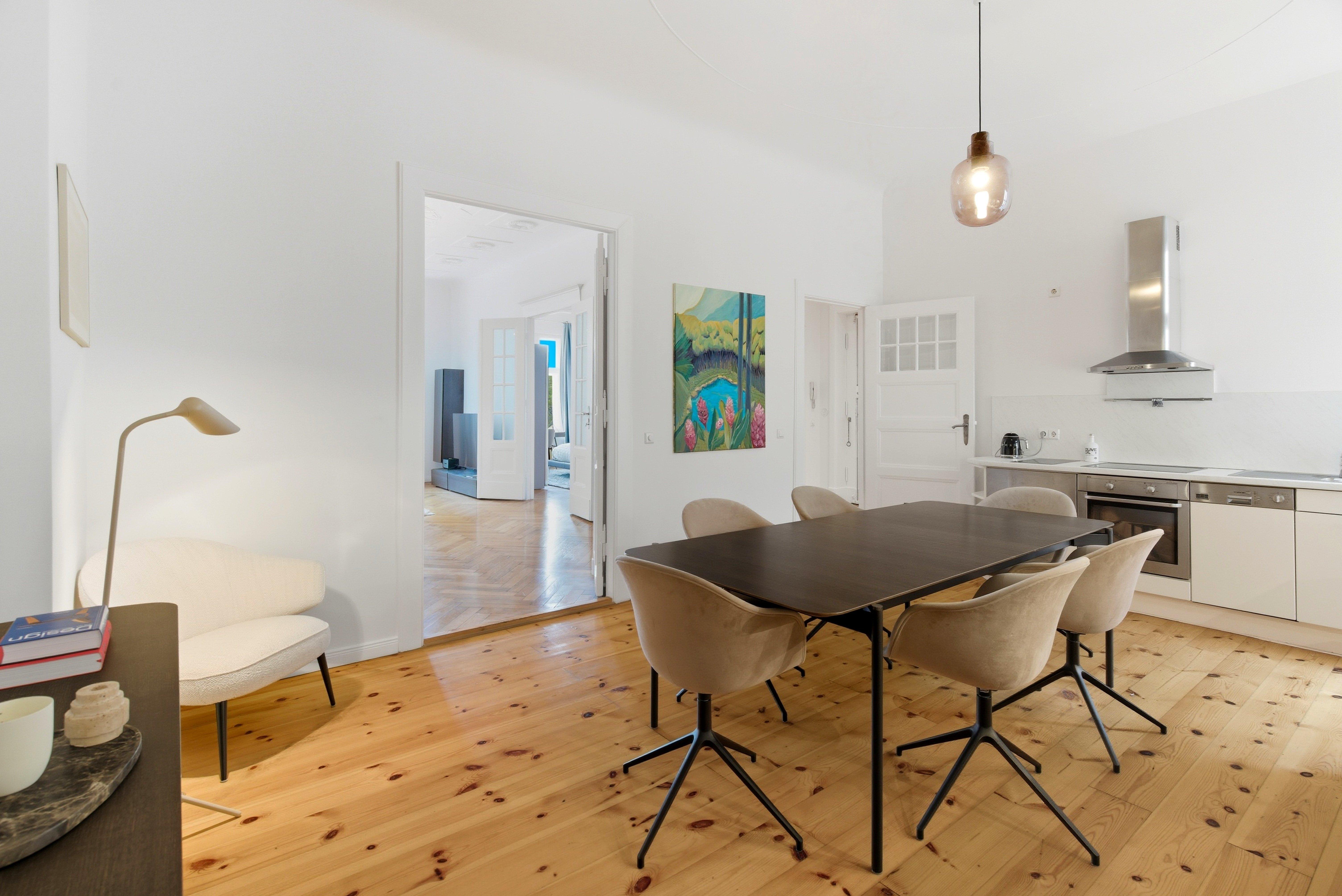 Salle à manger moderne avec table, chaises, cuisine équipée et tableau coloré.
