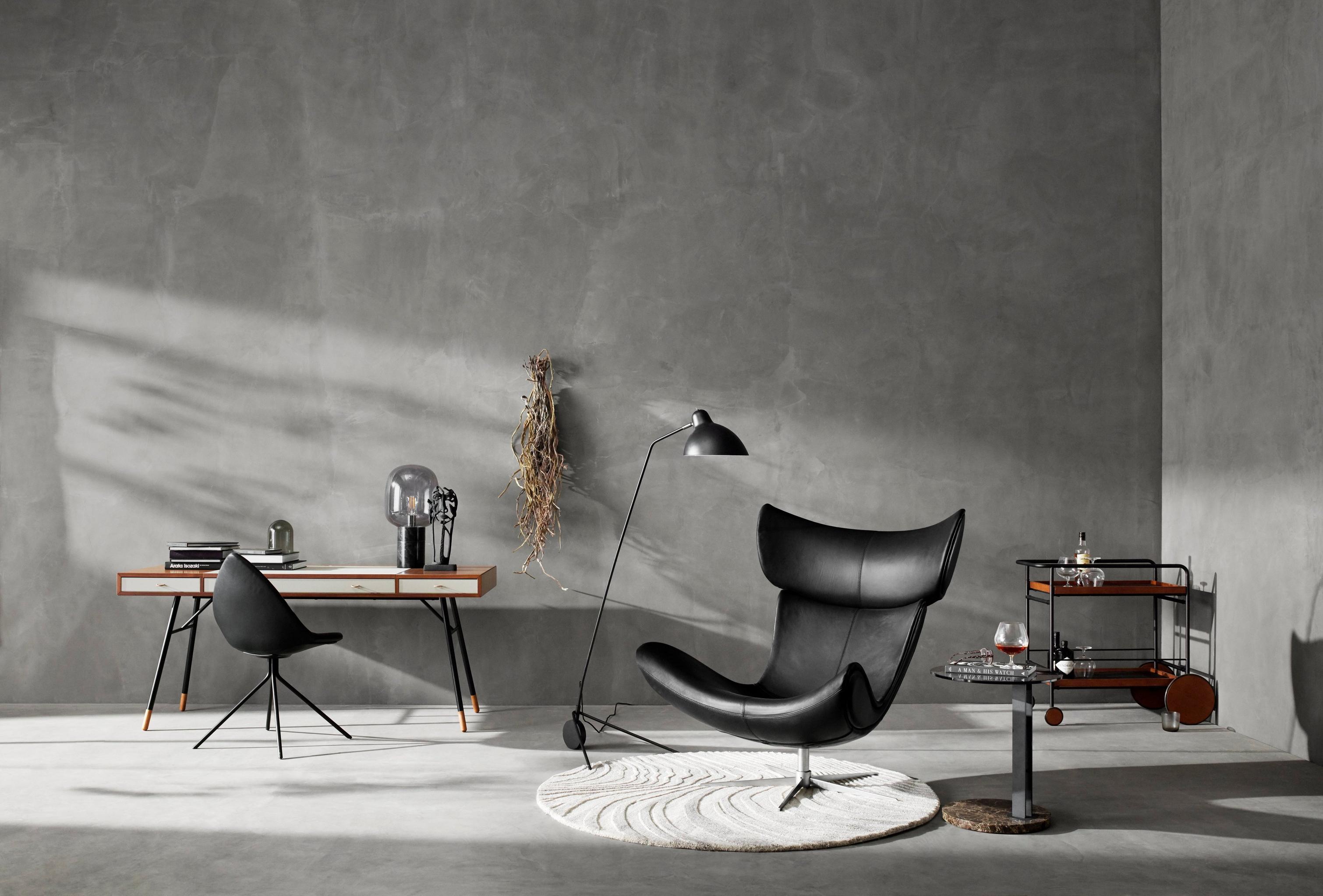 Chic office space with a black lounge chair, desk, lamp, and shelving against a grey textured wall.