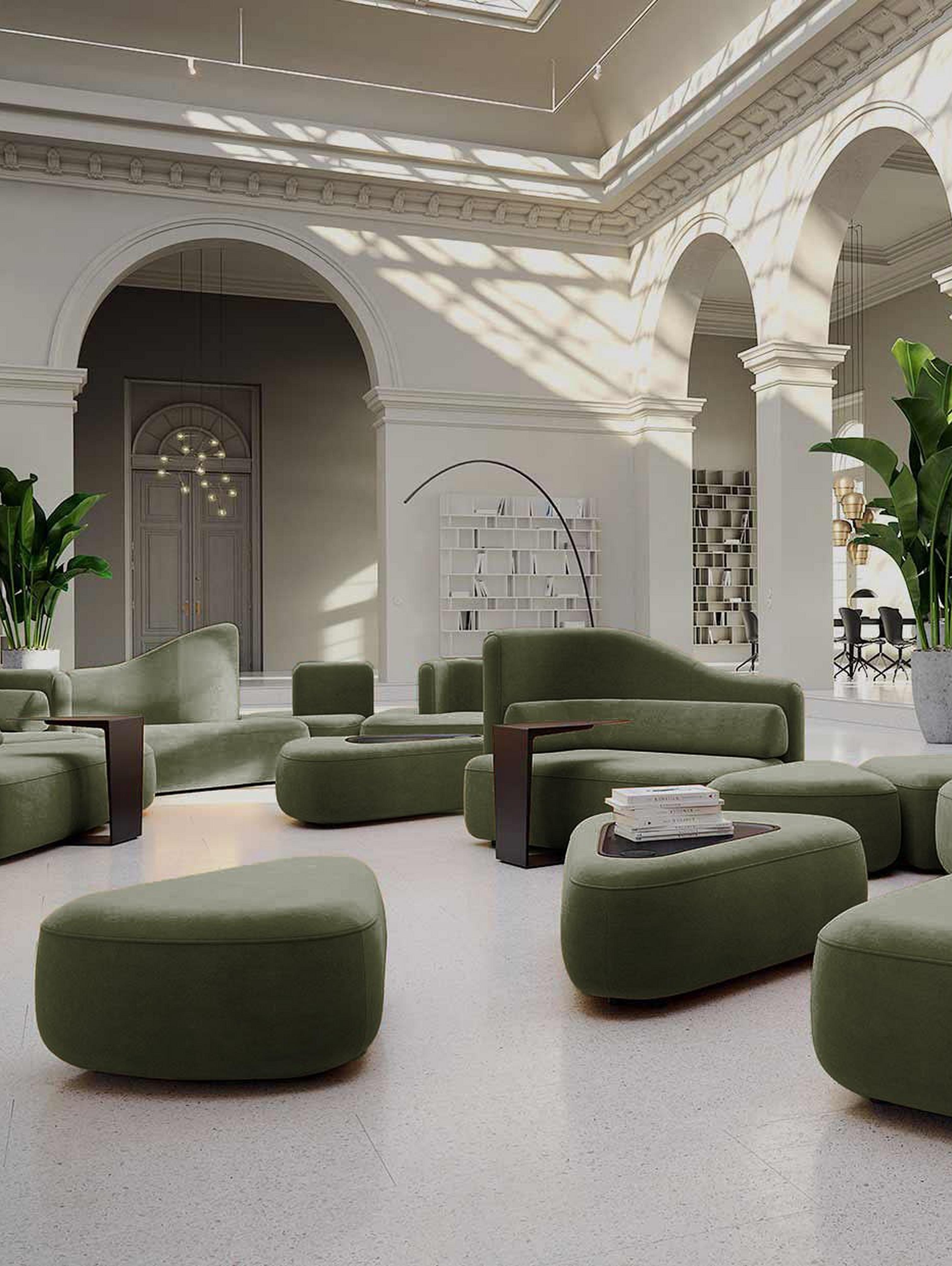 Spacious room with green sofas, white columns, arches, and potted plants in a bright setting.