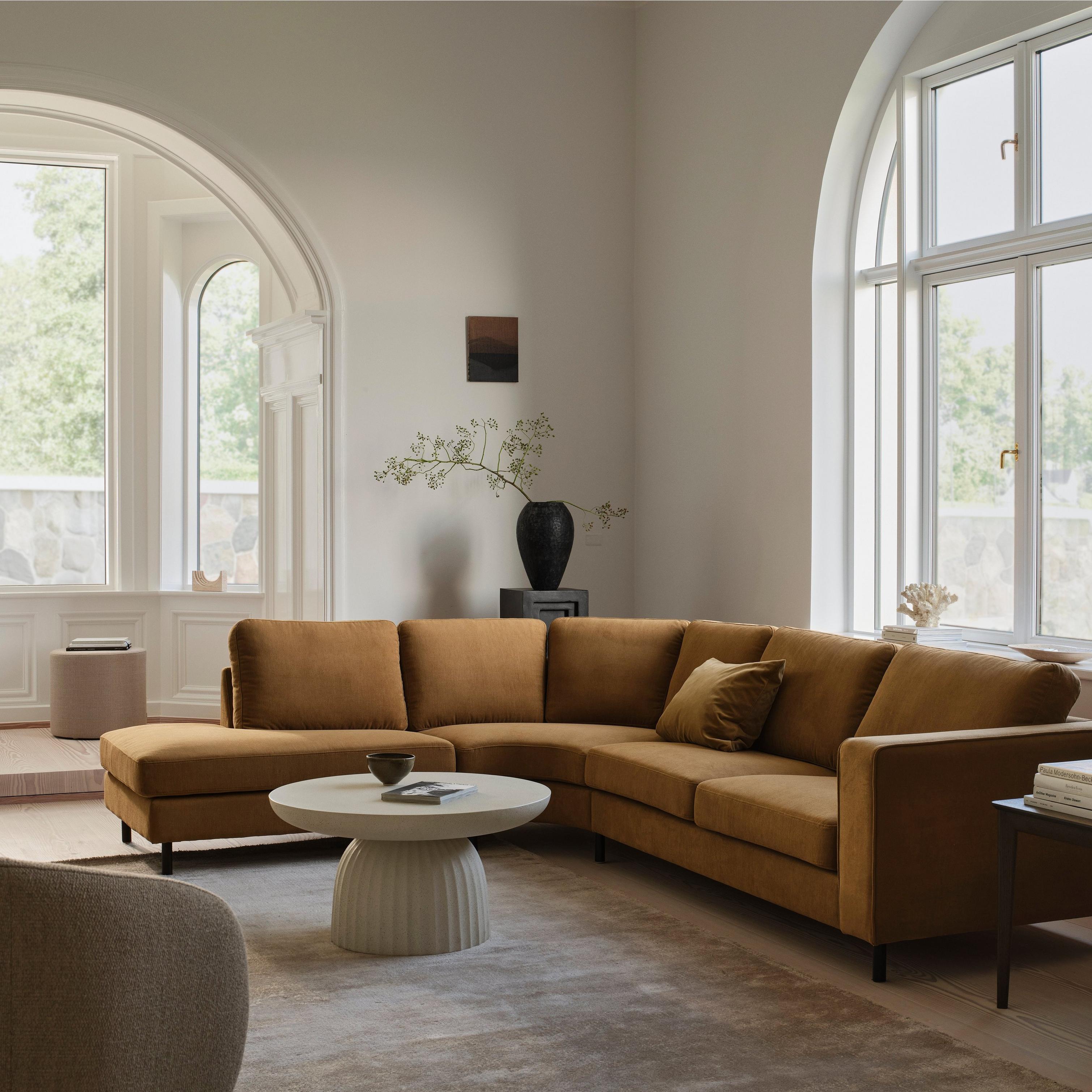 Modern living room with a mustard corner sofa, round table, and large arched windows.