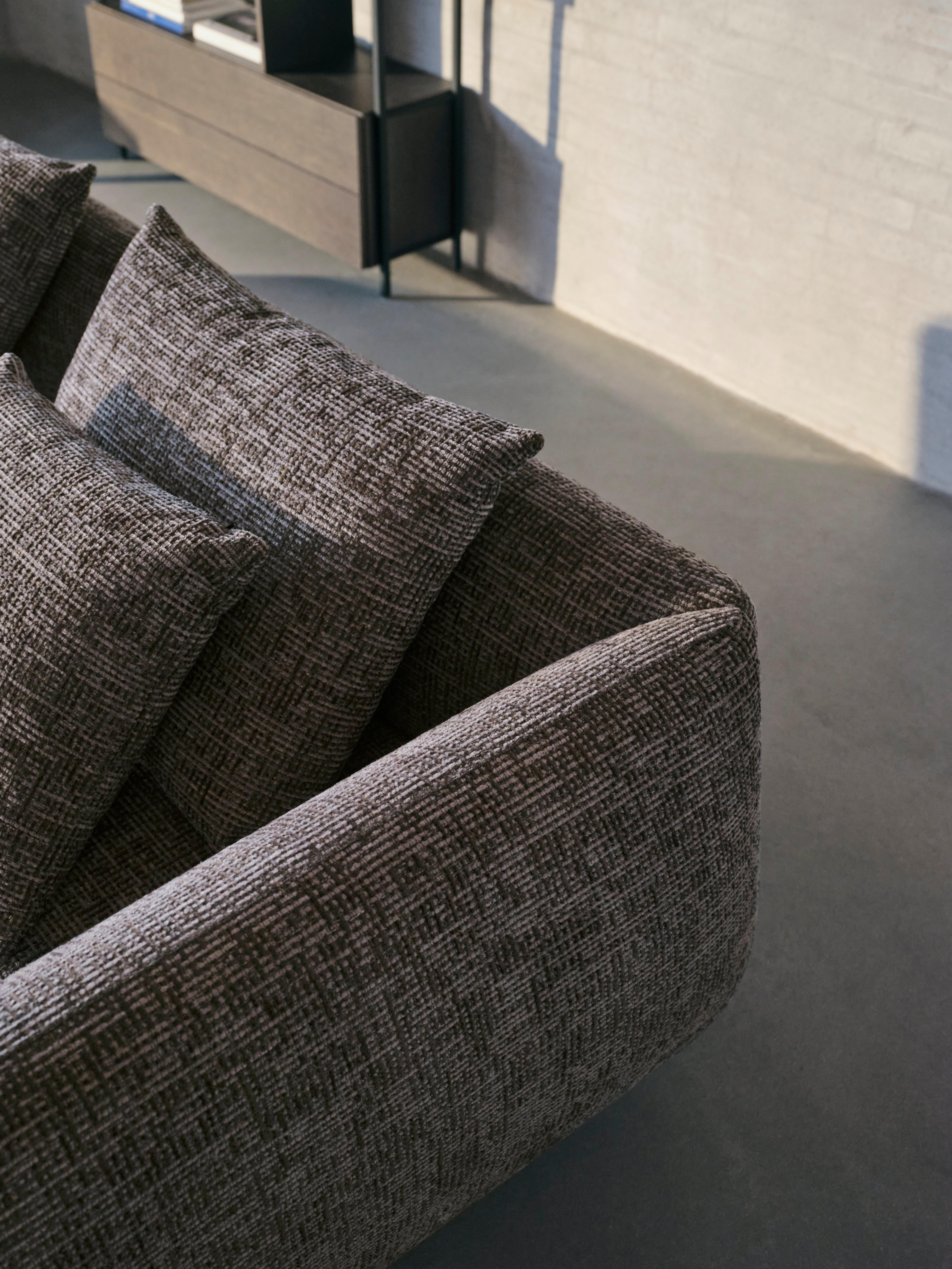 Rohová pohovka Salamanca čalouněná hnědou látkou Tuscany se širokými opěrkami rukou a polštáři vedle úložného systému Calgary z tmavé dubové dýhy.