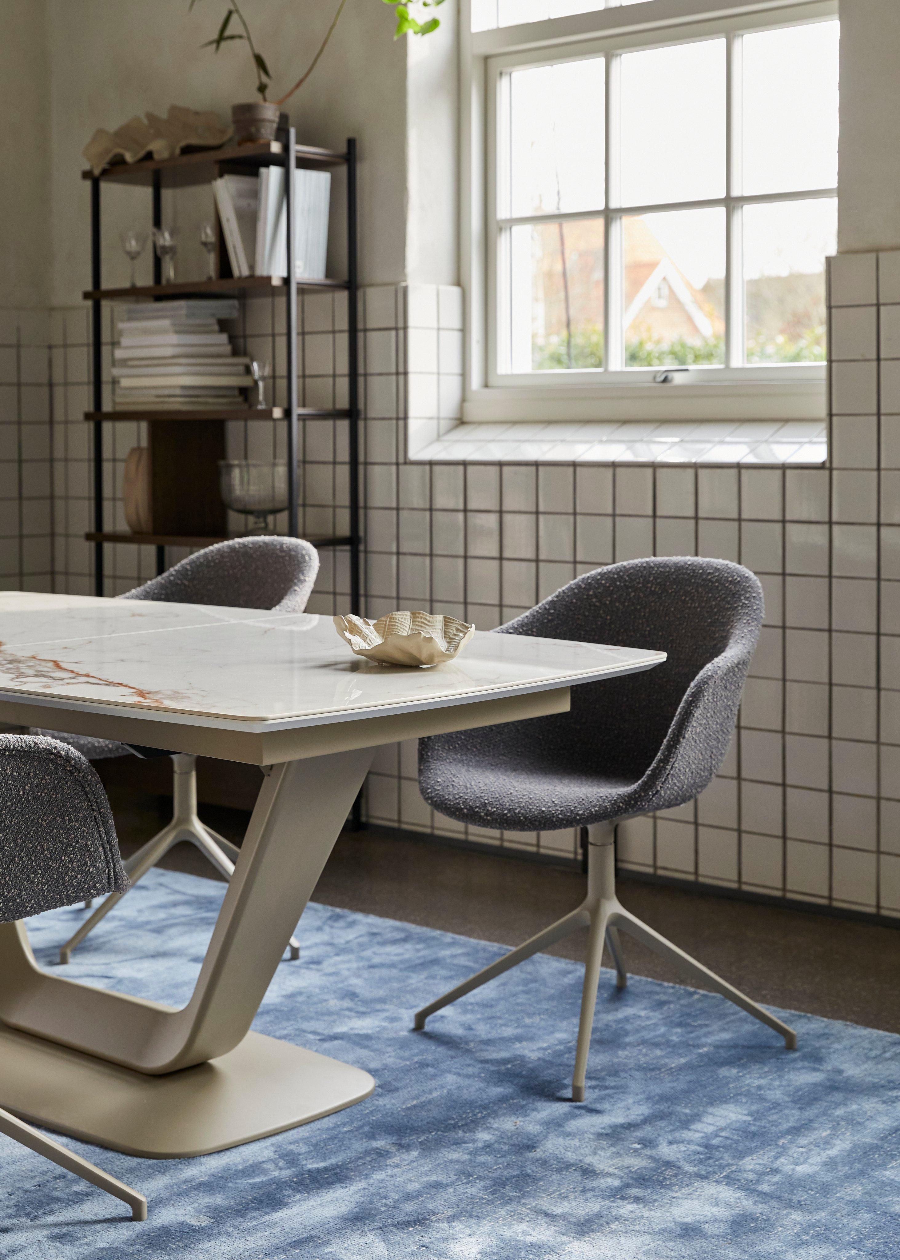 Table en marbre avec chaises grises sur tapis bleu, étagère et fenêtre en arrière-plan.