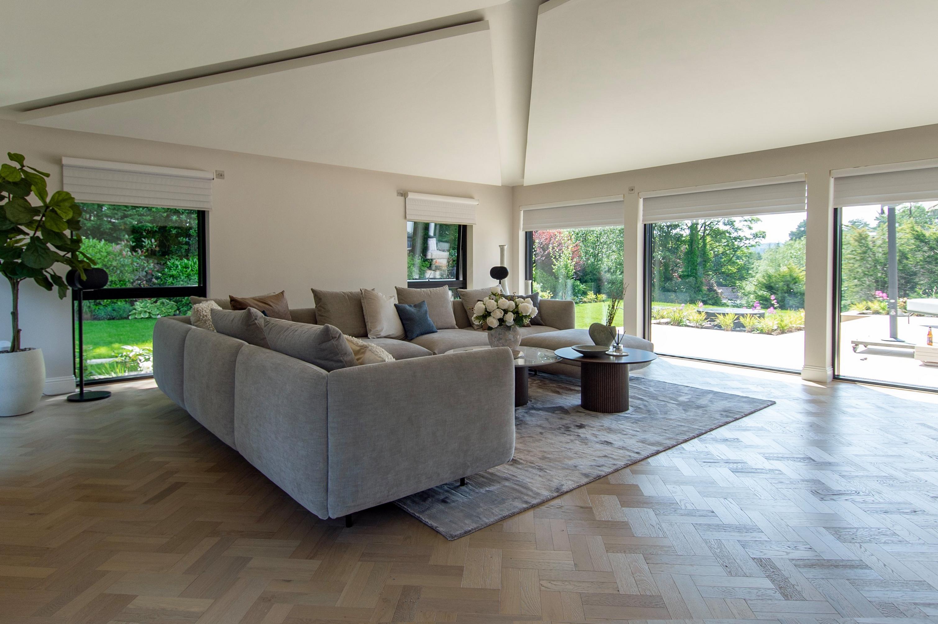 Modern living room with a grey sectional sofa, large windows, and a view of a garden.