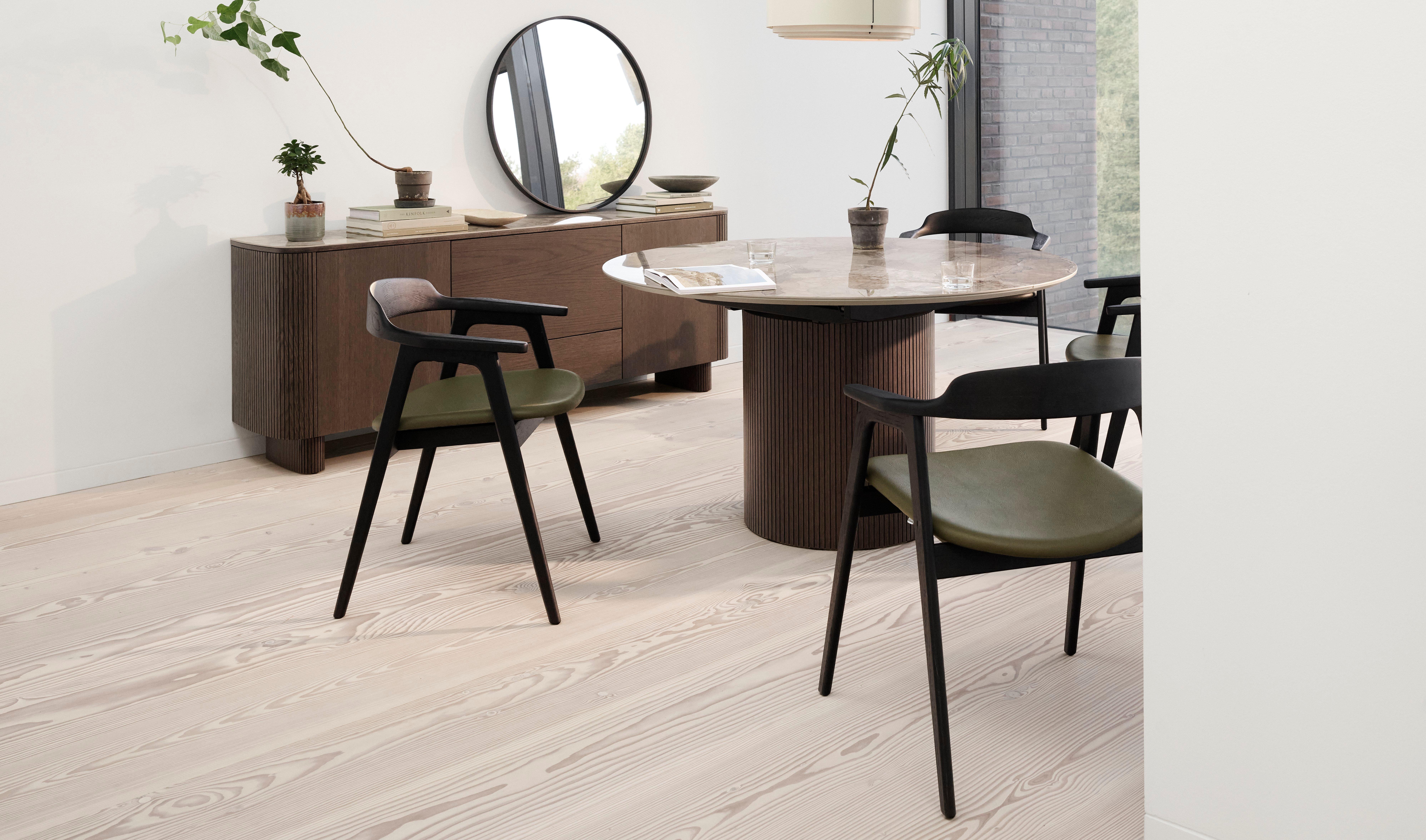 Minimalistisches Esszimmer mit ausziehbarem Santiago Esstisch mit Marmorplatte, Santiago Sideboard und Seoul Esszimmerstühlen mit grünen Kissen. Dekoriert mit einer Bubble Vase, einer Ribbon Vase und einer Paddle Pendelleuchte. Der Raum hat einen runden Spiegel auf dem Sideboard und grosse Fenster.