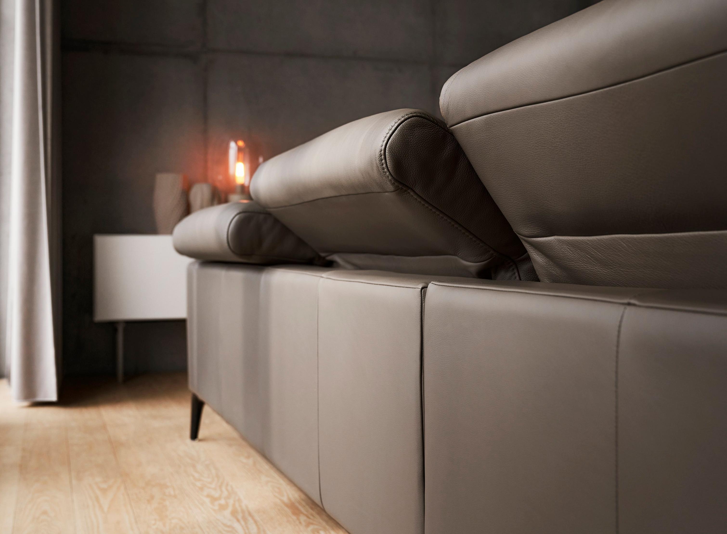 Vista lateral de un sofá en piel gris con iluminación suave y decoración minimalista.