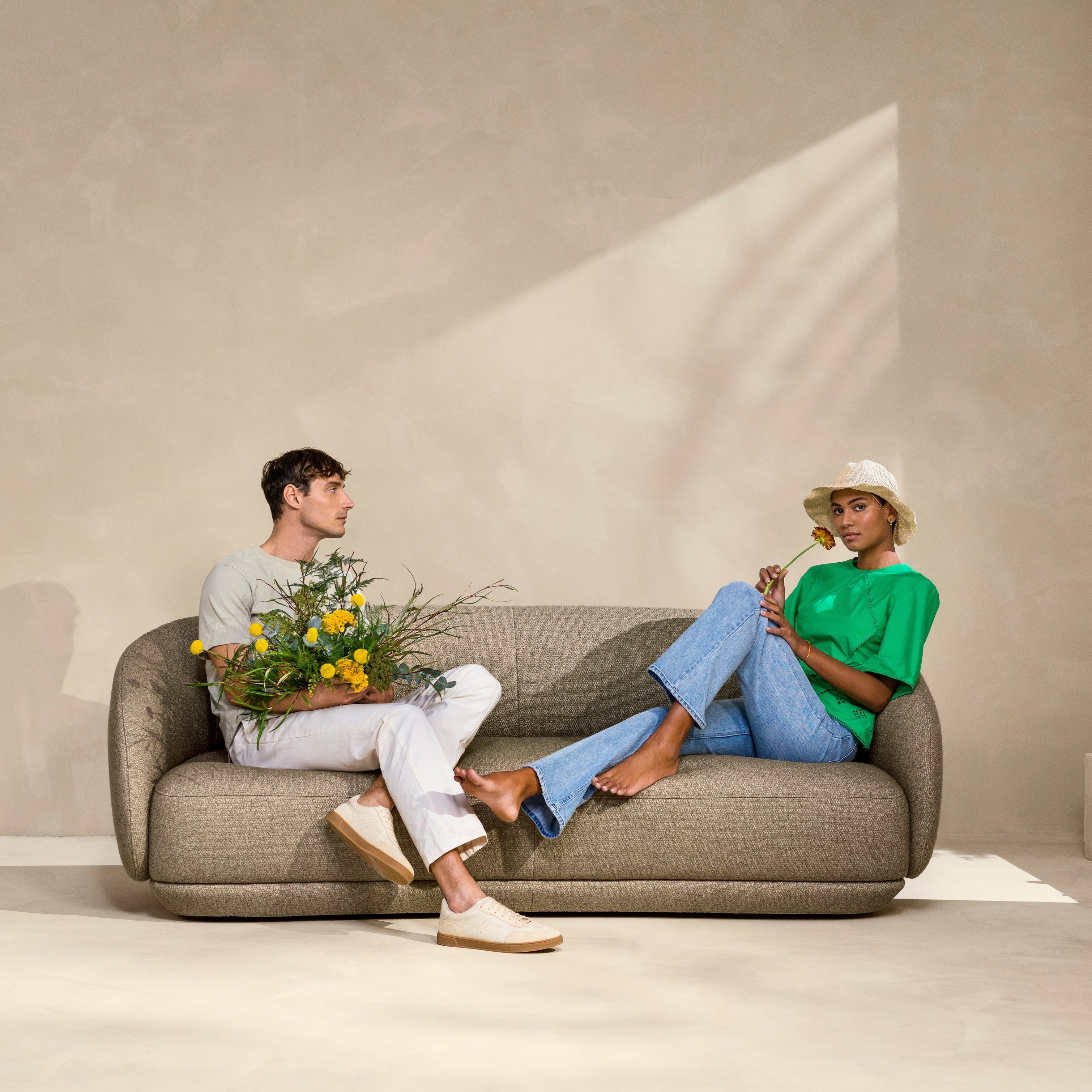 Пара сидит на диване Bolzano, обитом тканью Lazio коричневого цвета.