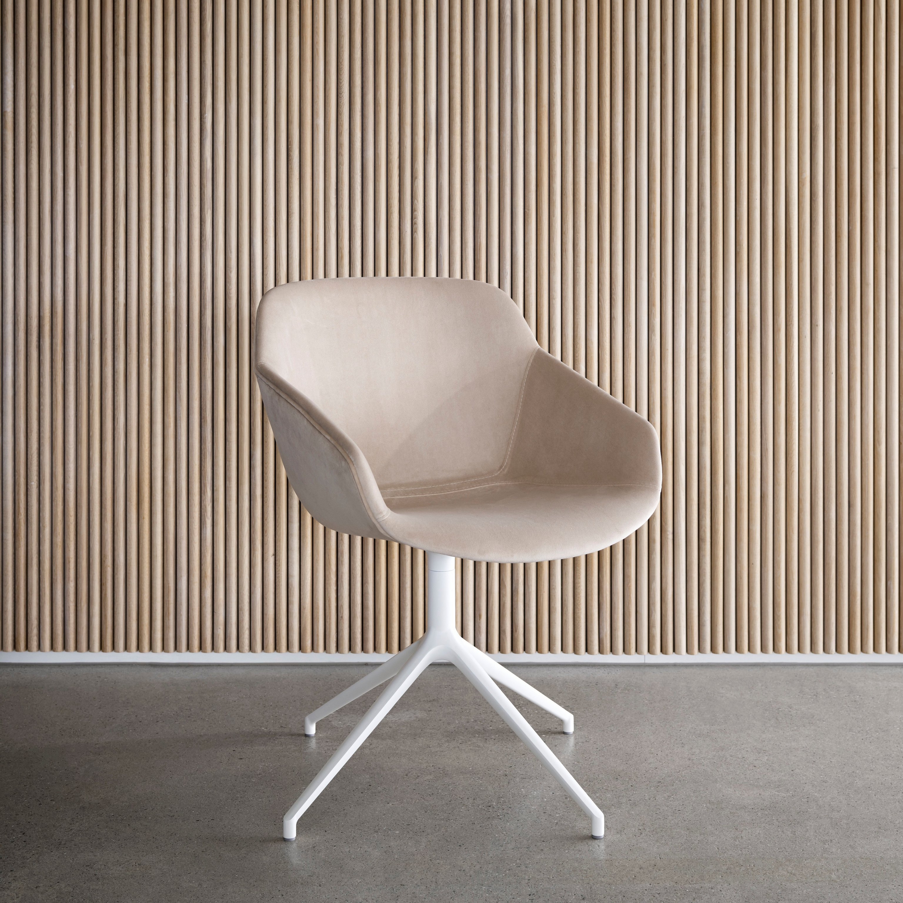 Tapicerowane beżową tkaniną krzesło z białą podstawą na tle ściany z pionowych drewnianych lameli.