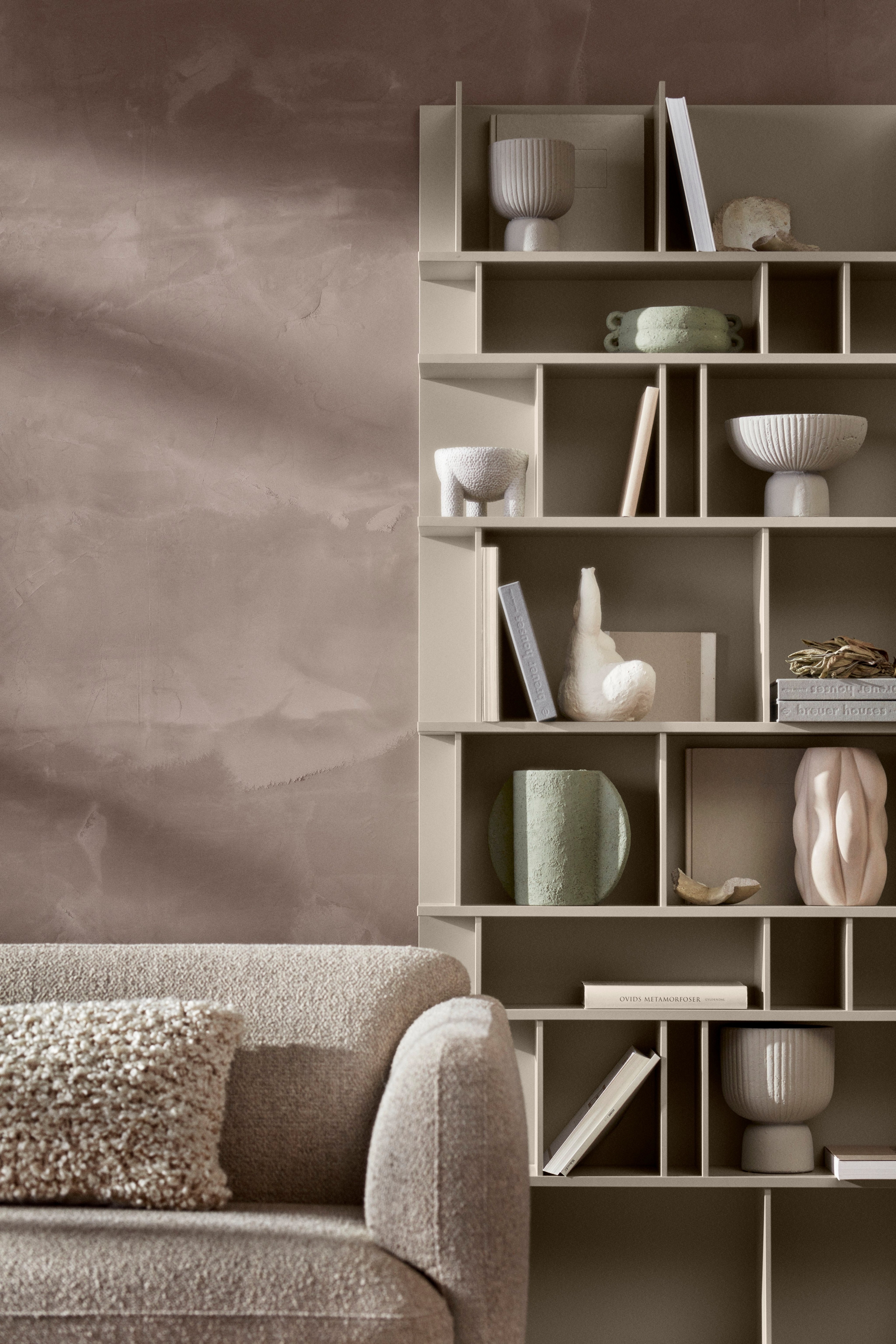 A modena sofa with a textured cushion and como shelving unit displaying assorted decorative items.