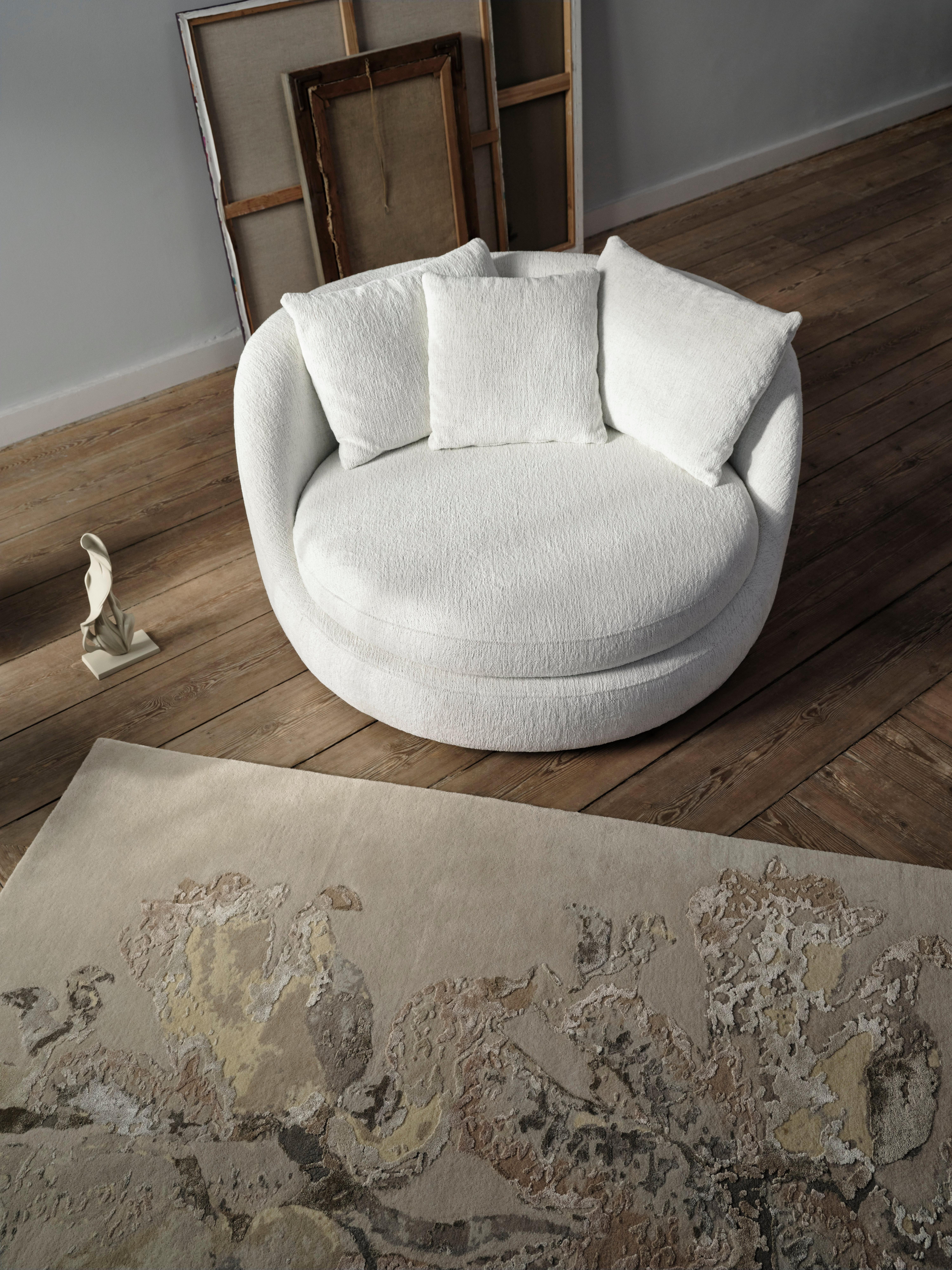 Flora 7 beige rug with floral pattern beside white circular armchair and warm grey Flora 4 sculpture on wood floor.
