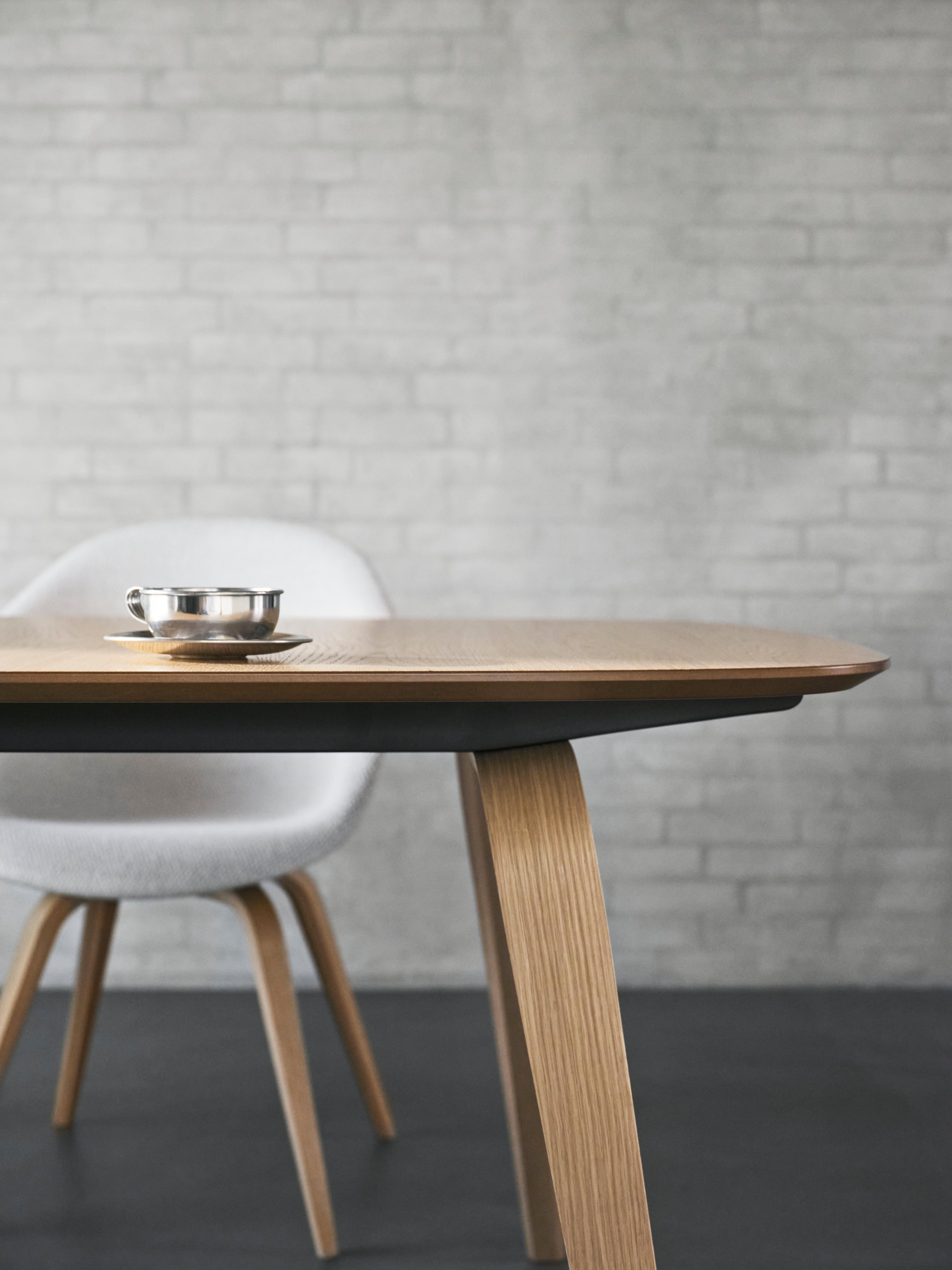 Close-up of Hauge dining table in natural oak veneer with Hauge dining chair in white Lazio fabric, set against a light brick wall.