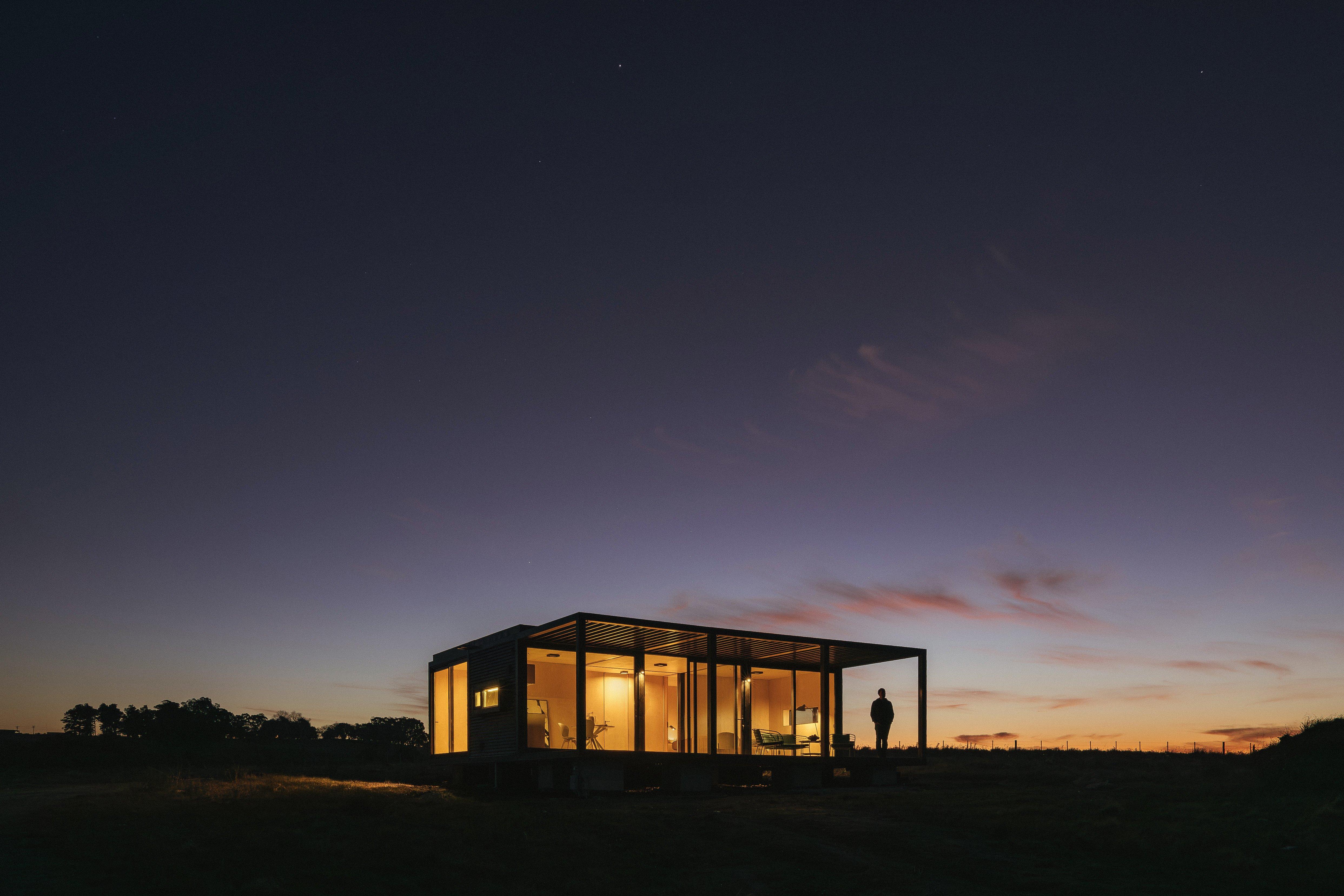 玻璃屋內燈光明亮，人在屋外站立，背景是黃昏天空。