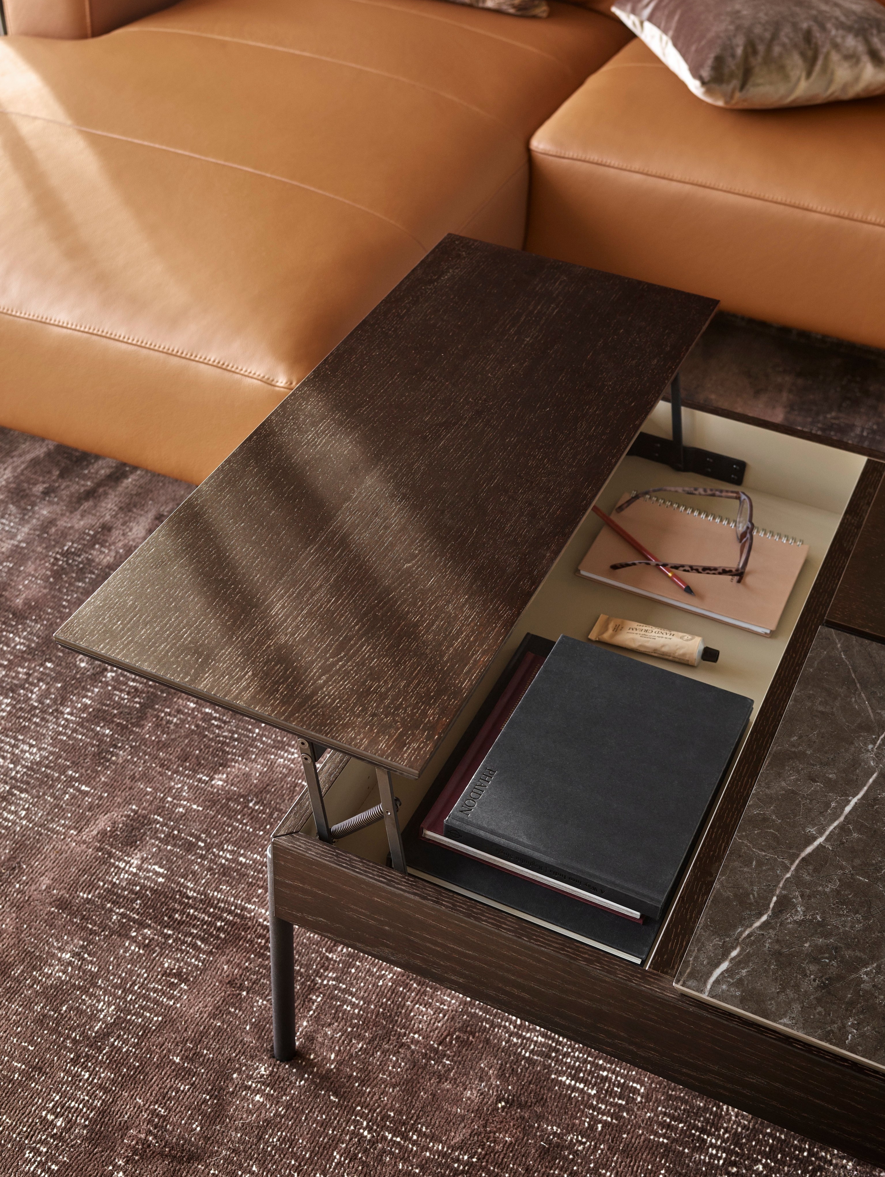 Close-up of a modern Chiva coffee table with books and accessories, near a tan leather sofa.