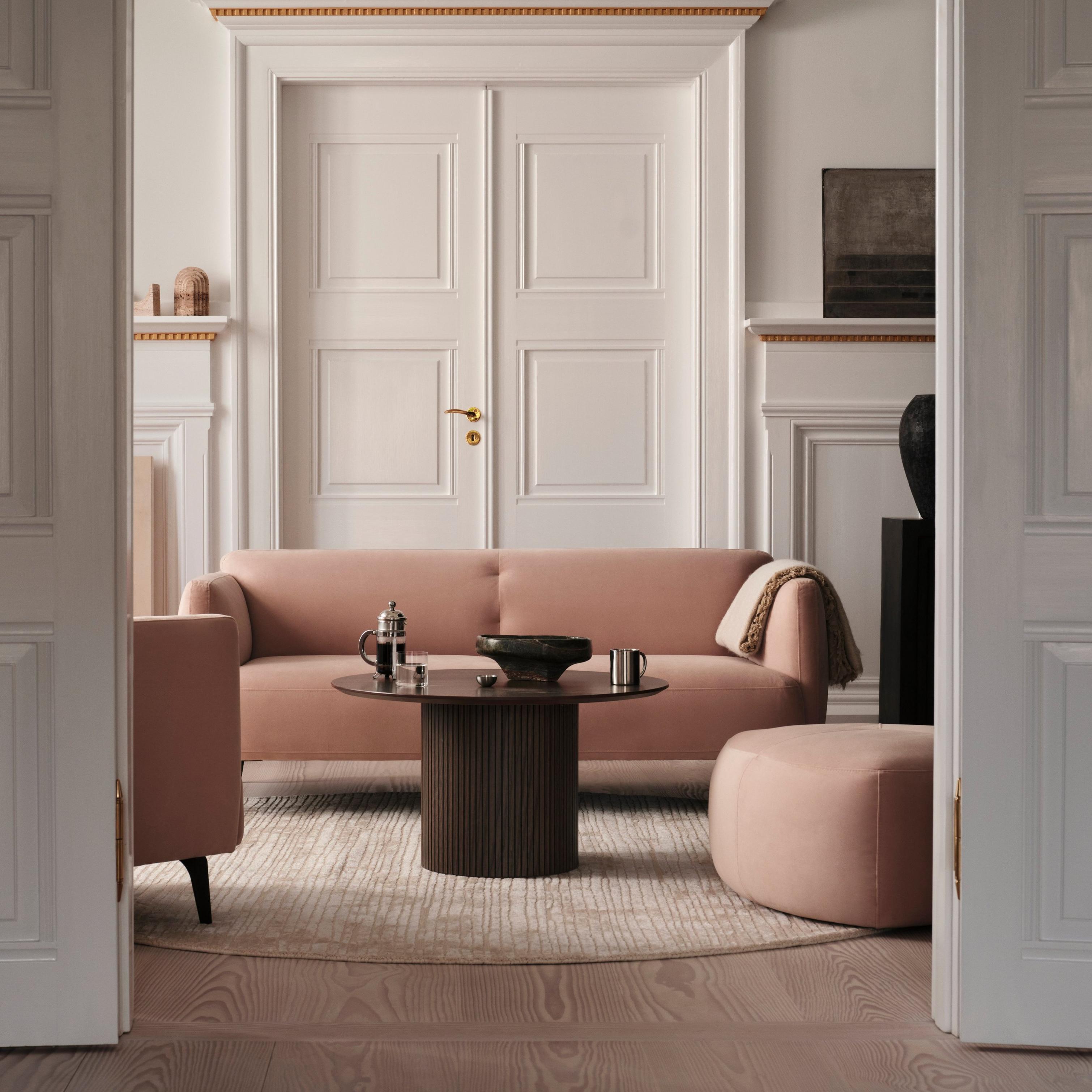 Elegant living room with a pink sofa, coffee table, and pouf on a round rug.