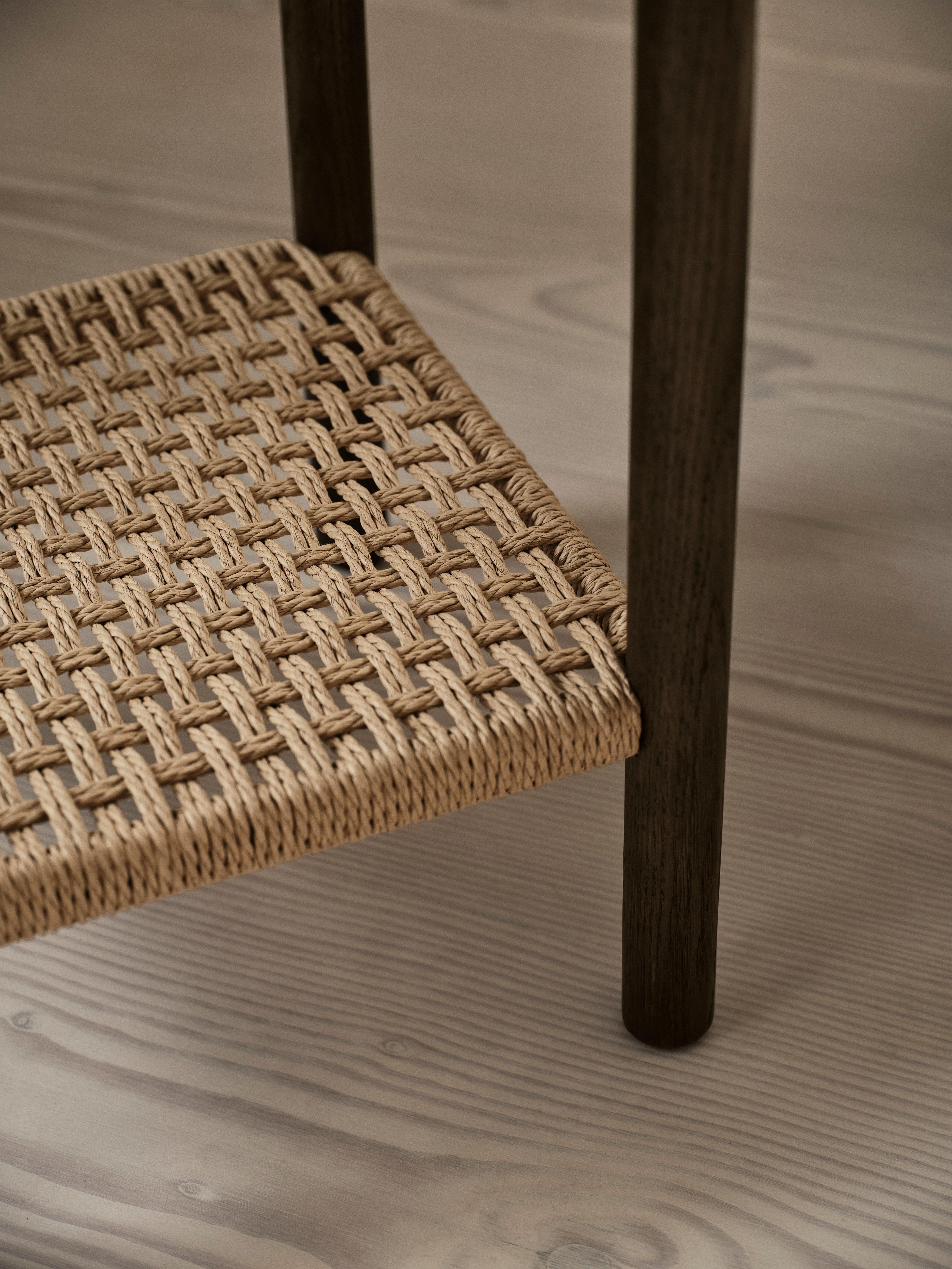 Woven rattan seat with dark wooden legs on a light wooden floor.