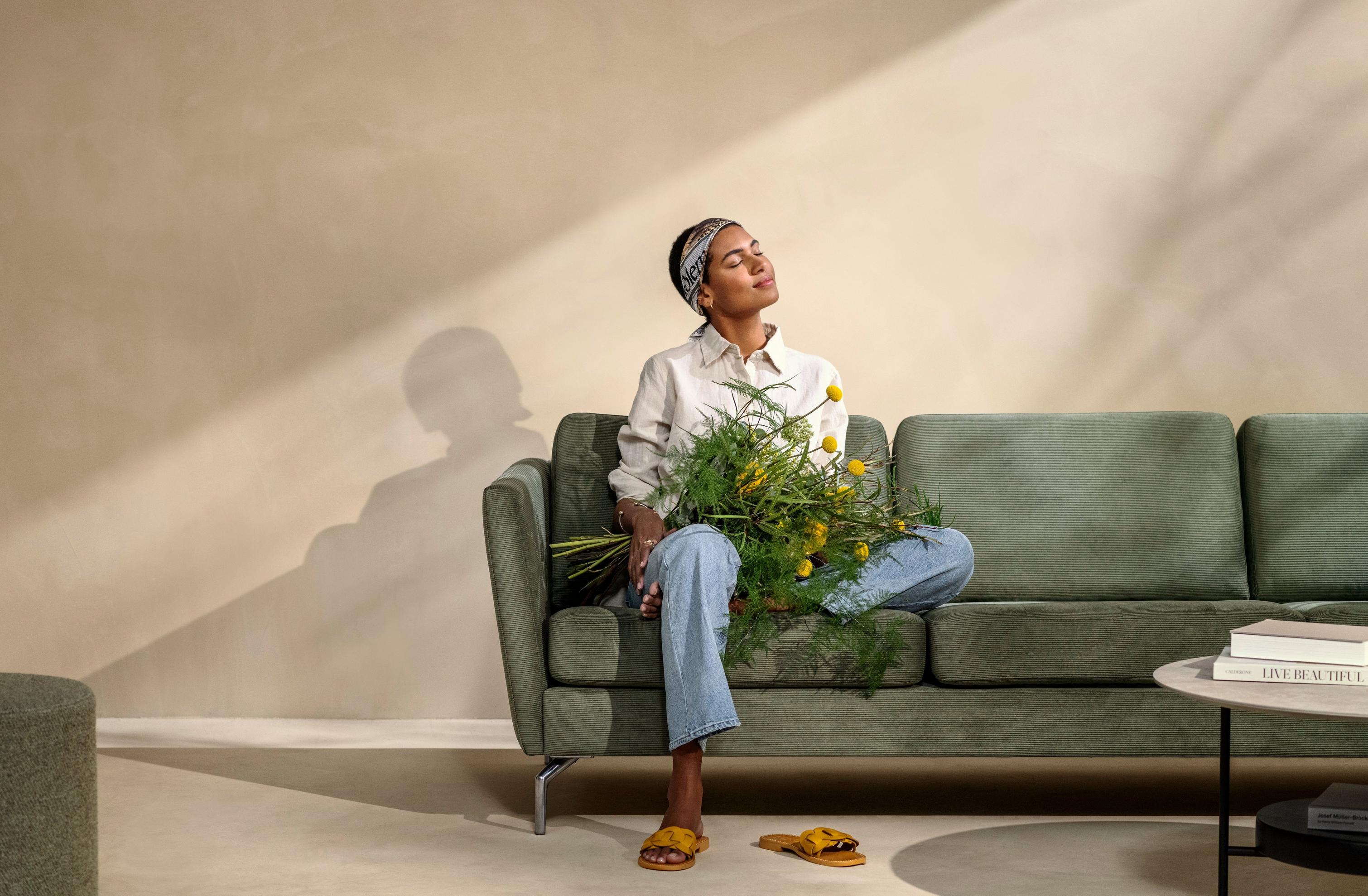 グリーンのSkagen ファブリックを使ったOsaka ソファに座り、花を抱える女性。