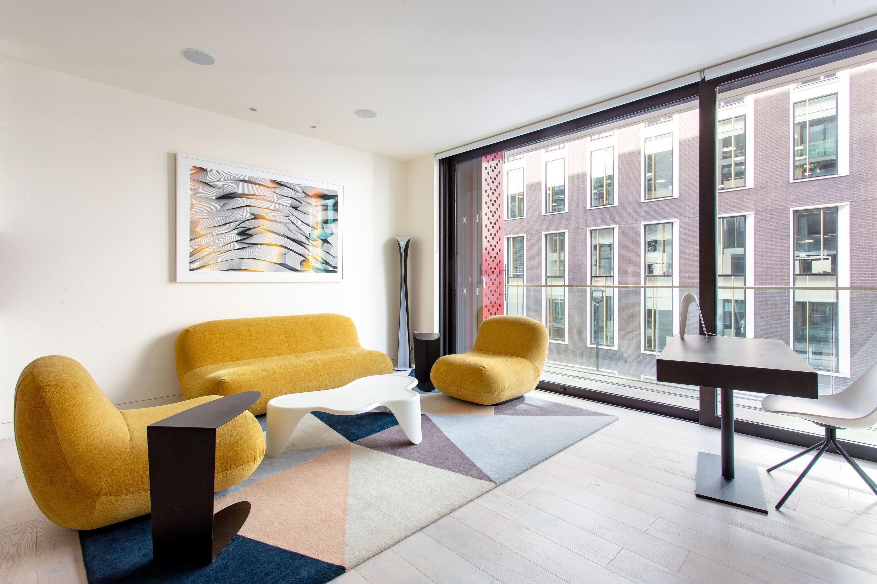 Bright living space with Golden Chelsea chairs, wall art, and city view window.