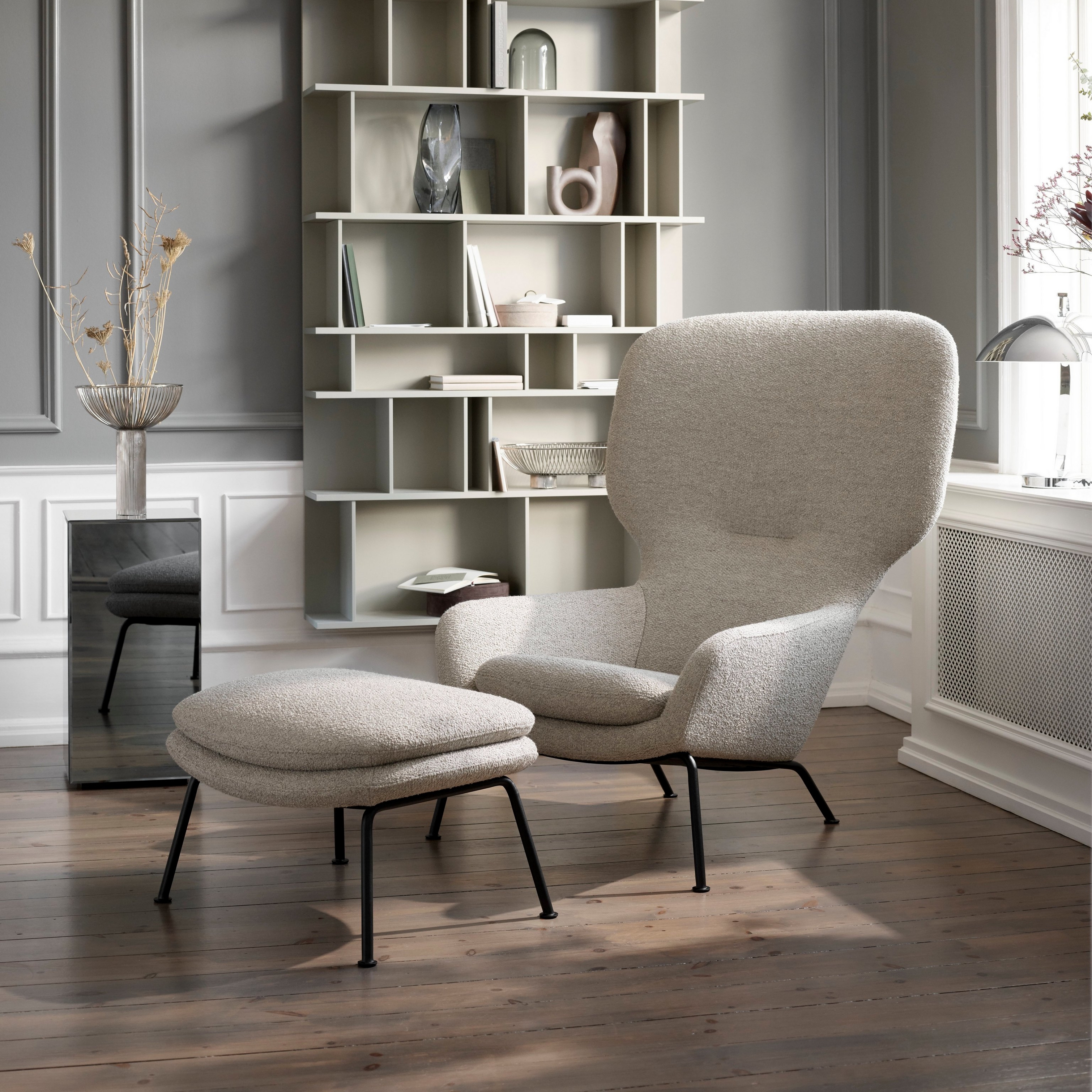 Lounge chair and ottoman with bookshelf and decor, in a classic room with dark floors.