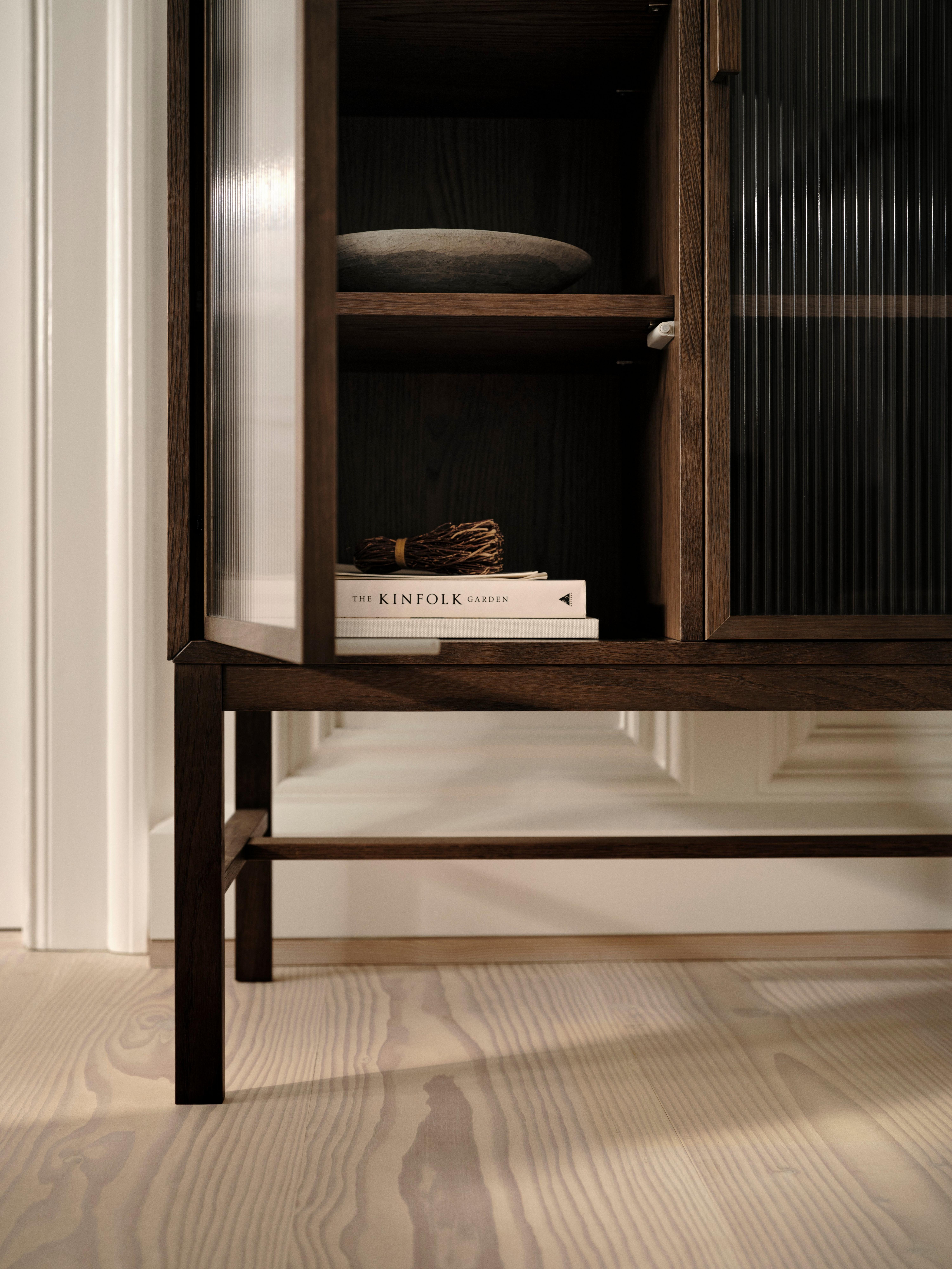 Holzschrank mit Glasfront, darin ein Buch "The Kinfolk Garden" und eine Schale auf Holzregalen.