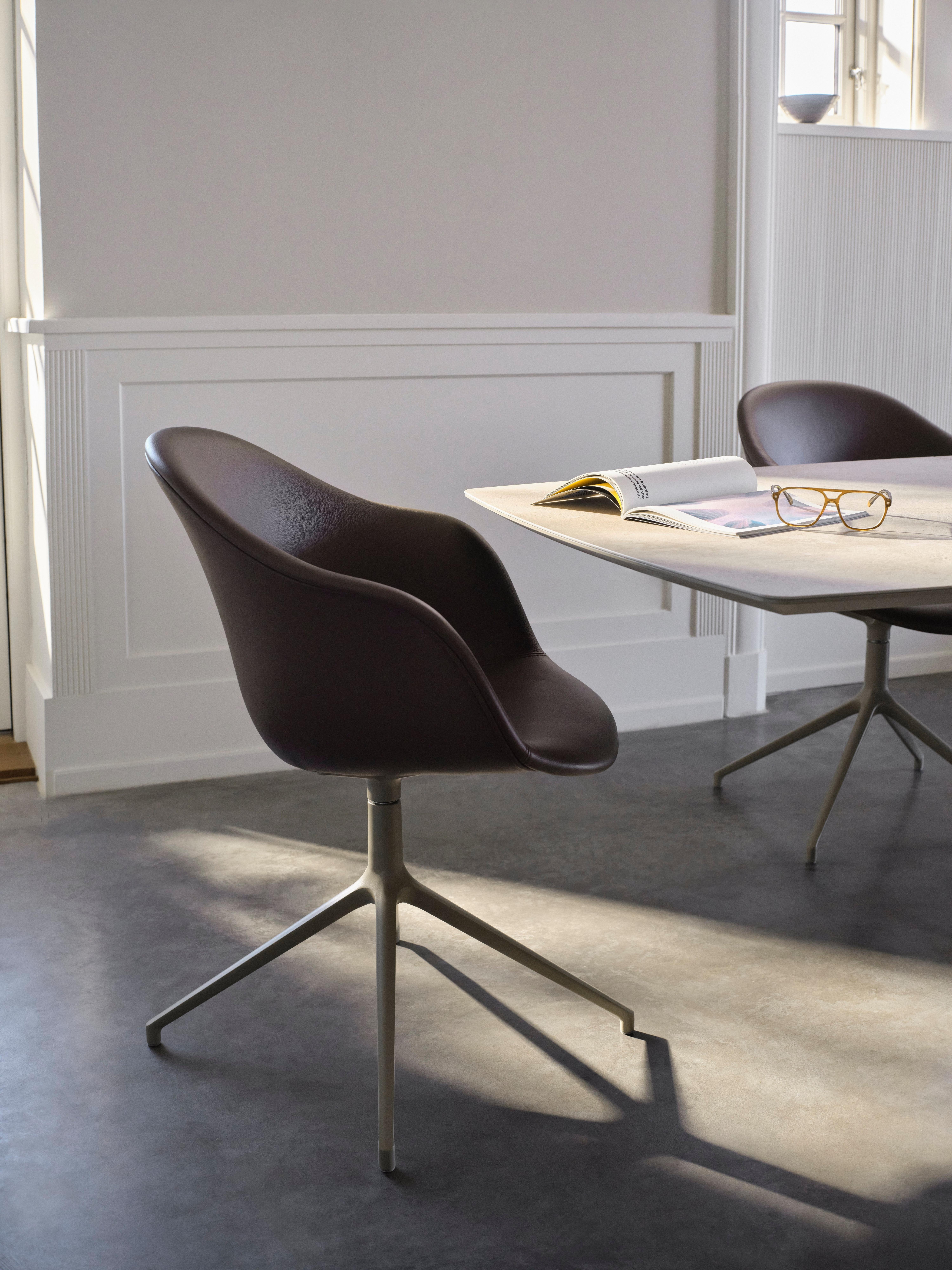 Der ausziehbare Alicante Esstisch aus Keramik in Aschgrau mit den Adelaide Esszimmerdrehstühlen aus steingrauem Nordic Grain Leder in einem hellen, minimalistischen Raum.