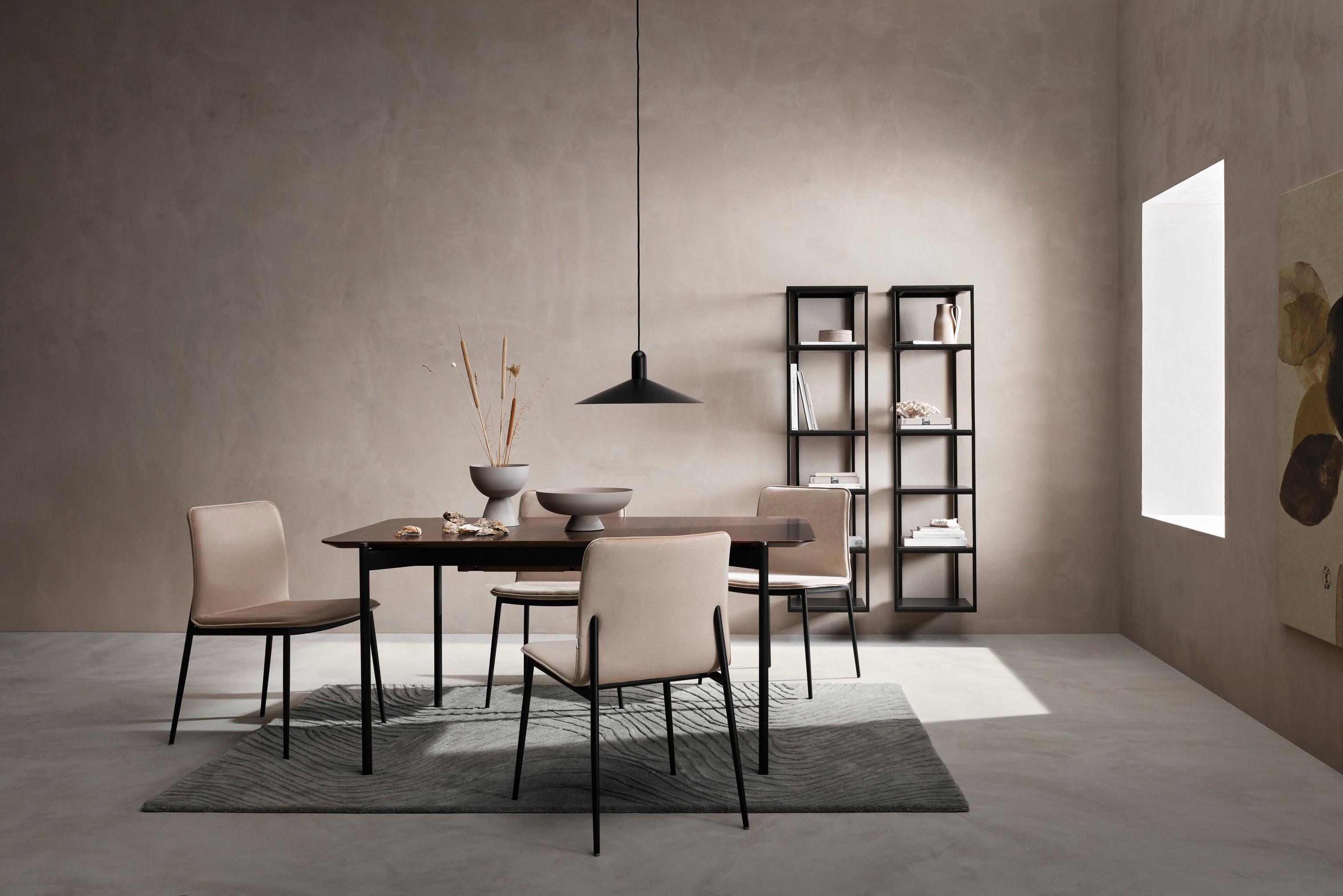 Minimalist dining area with tan chairs, wooden table, pendant lamp, and shelving against a grey wall.