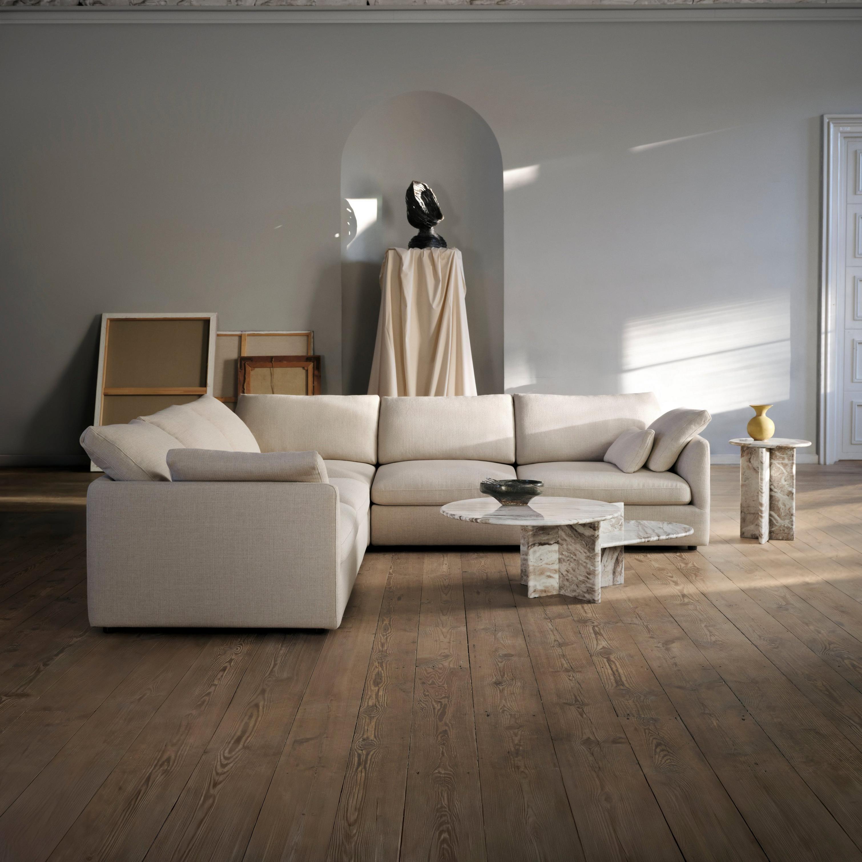Neutral-toned living room with light beige sectional sofa, marble tables, and classical wall relief above an arched niche with sculpture.