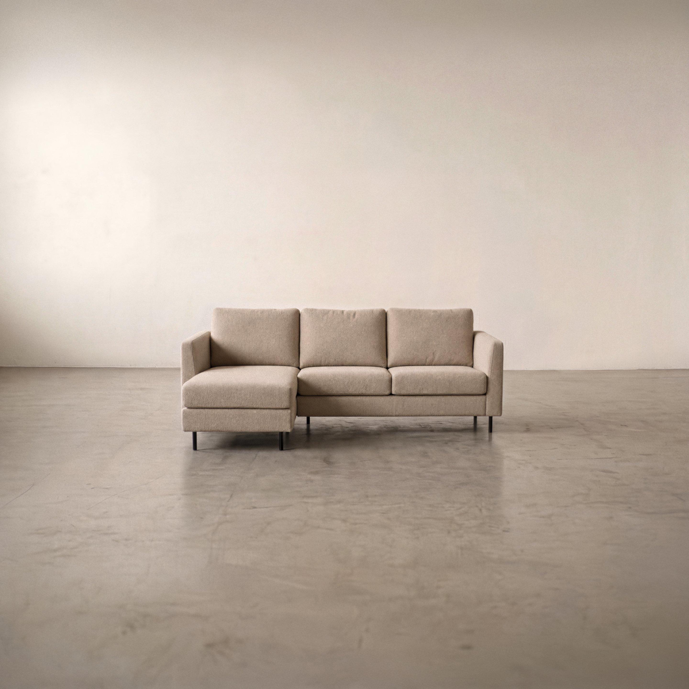 Sofá beige de tres plazas con chaise longue a la izquierda y patas negras.