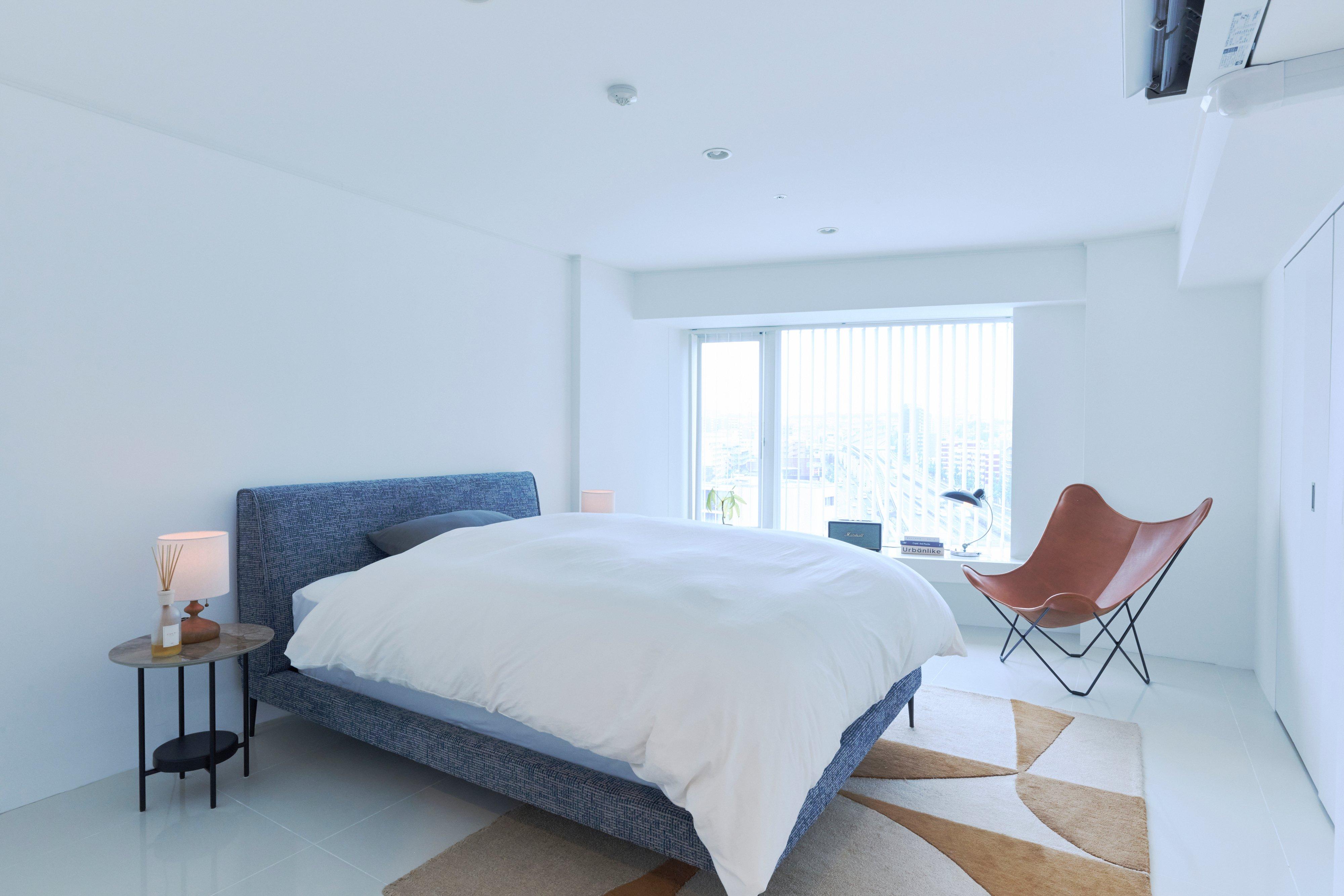 Modern bedroom with upholstered bed, bedside table with lamp, and leather chair by window.