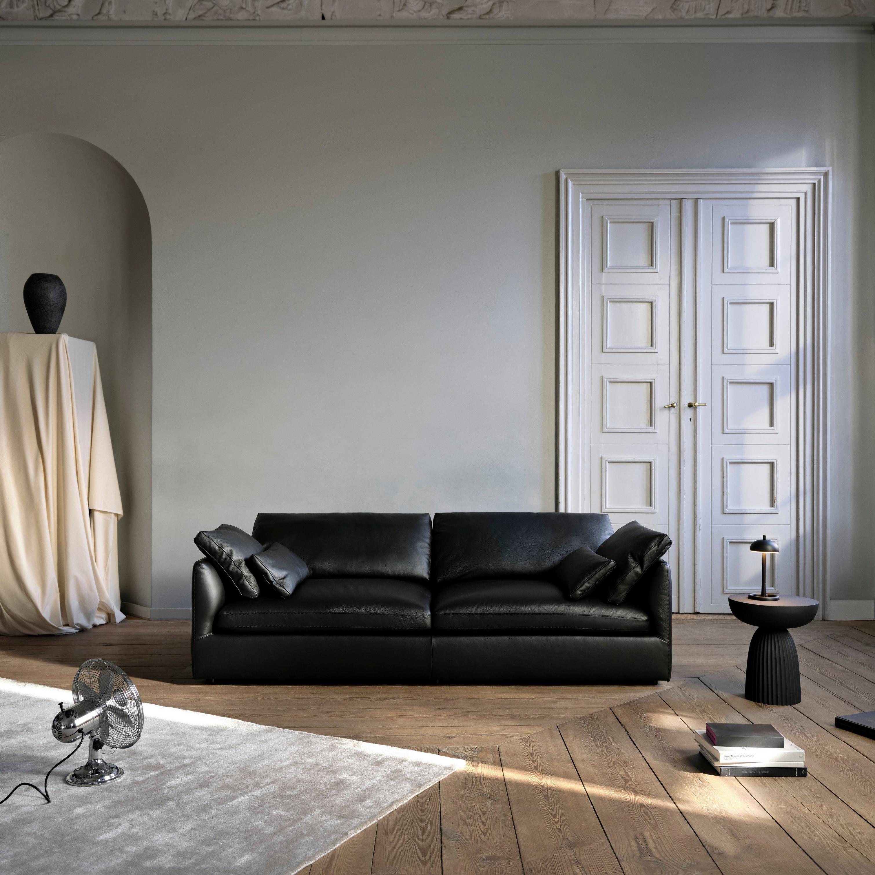 Black Paris table lamp on black Expose side table beside black sofa; Rubble vase on draped pedestal in classic interior.