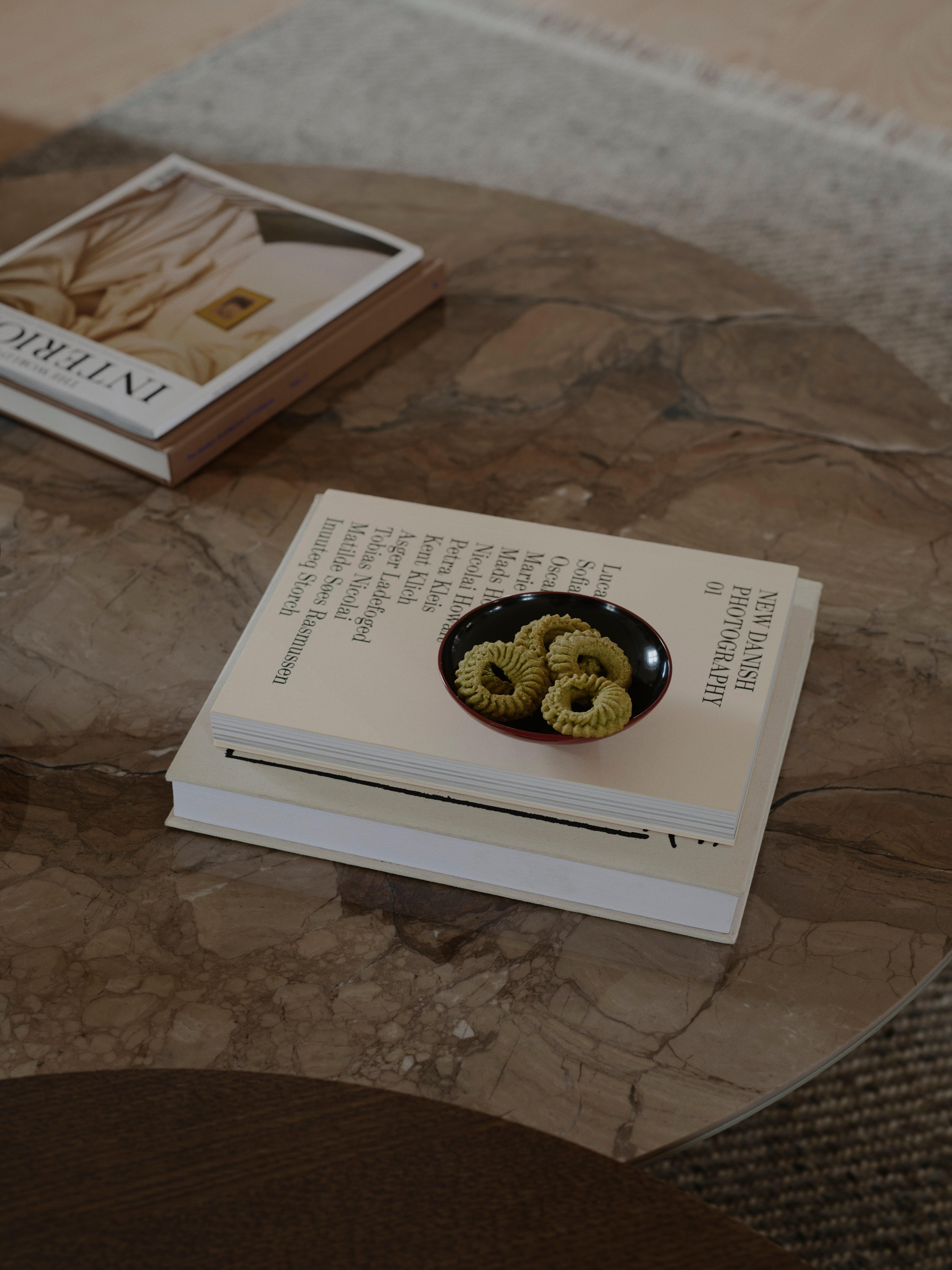 Small bowl of biscuits on stacked coffee-table books on a marble table.
