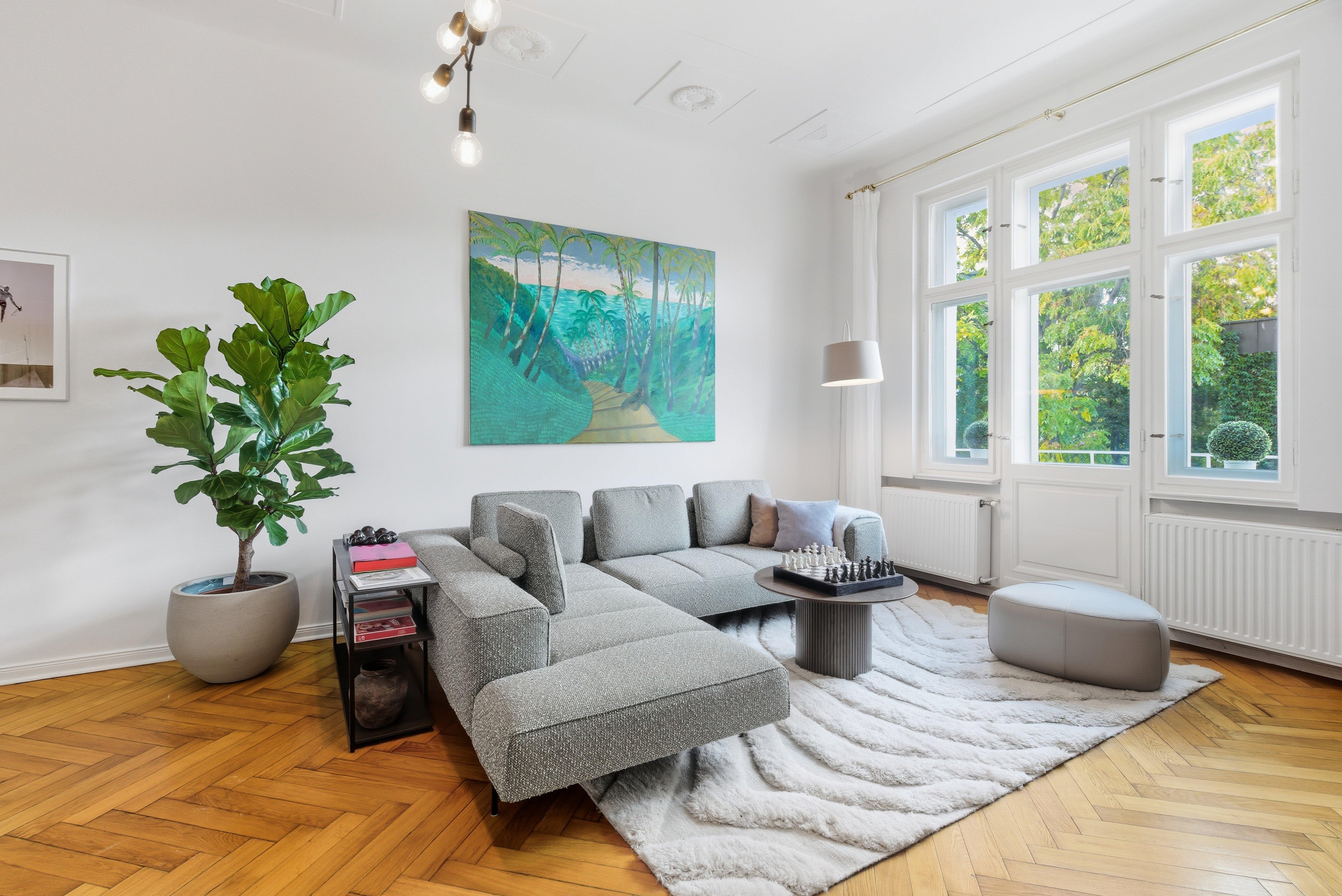 Salon moderne avec canapé gris, tapis blanc, plante en pot, et échiquier sur table basse.