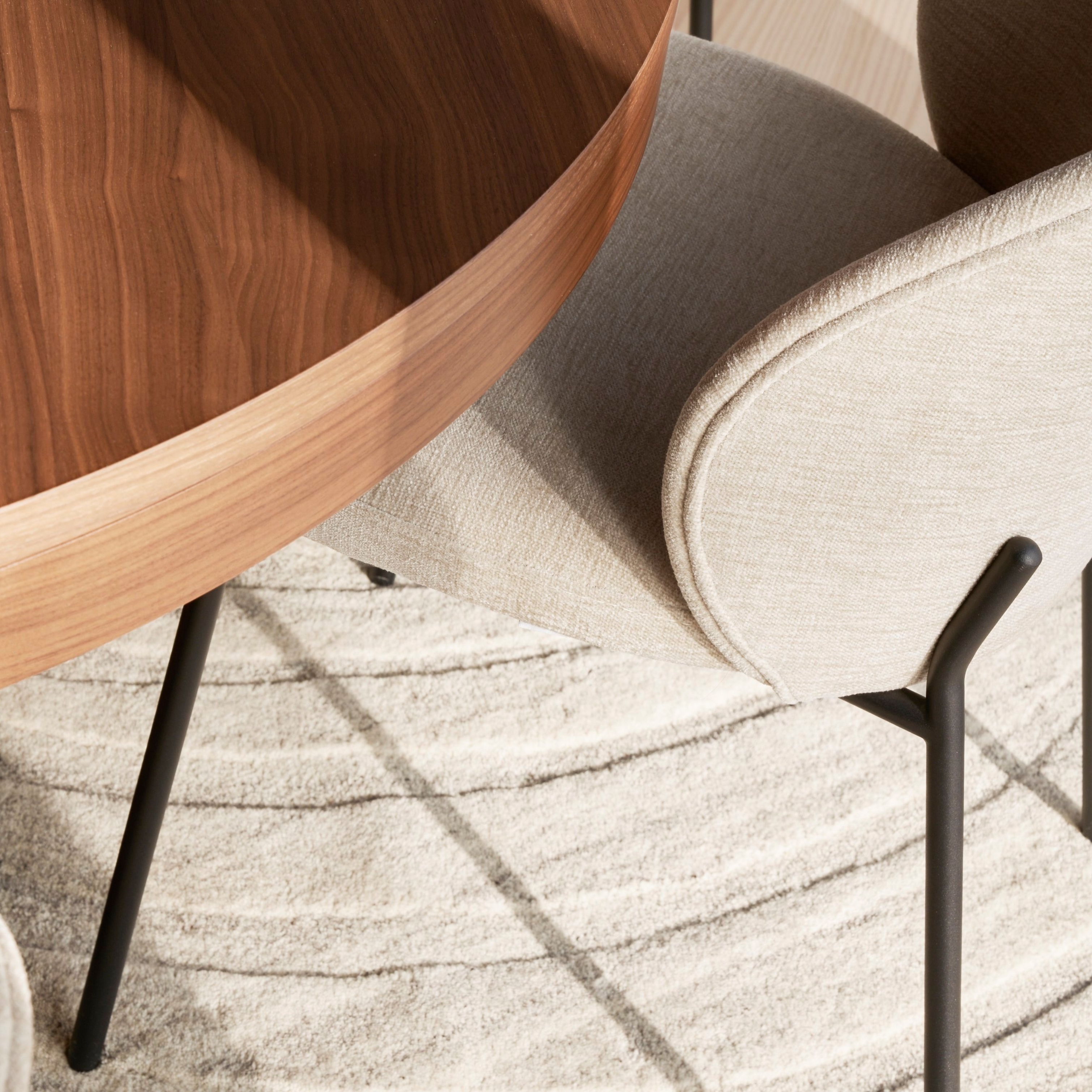 Nahaufnahme eines beigefarbenen gepolsterten Princeton Stuhls und eines runden Holztisches auf einem gemusterten Teppich.