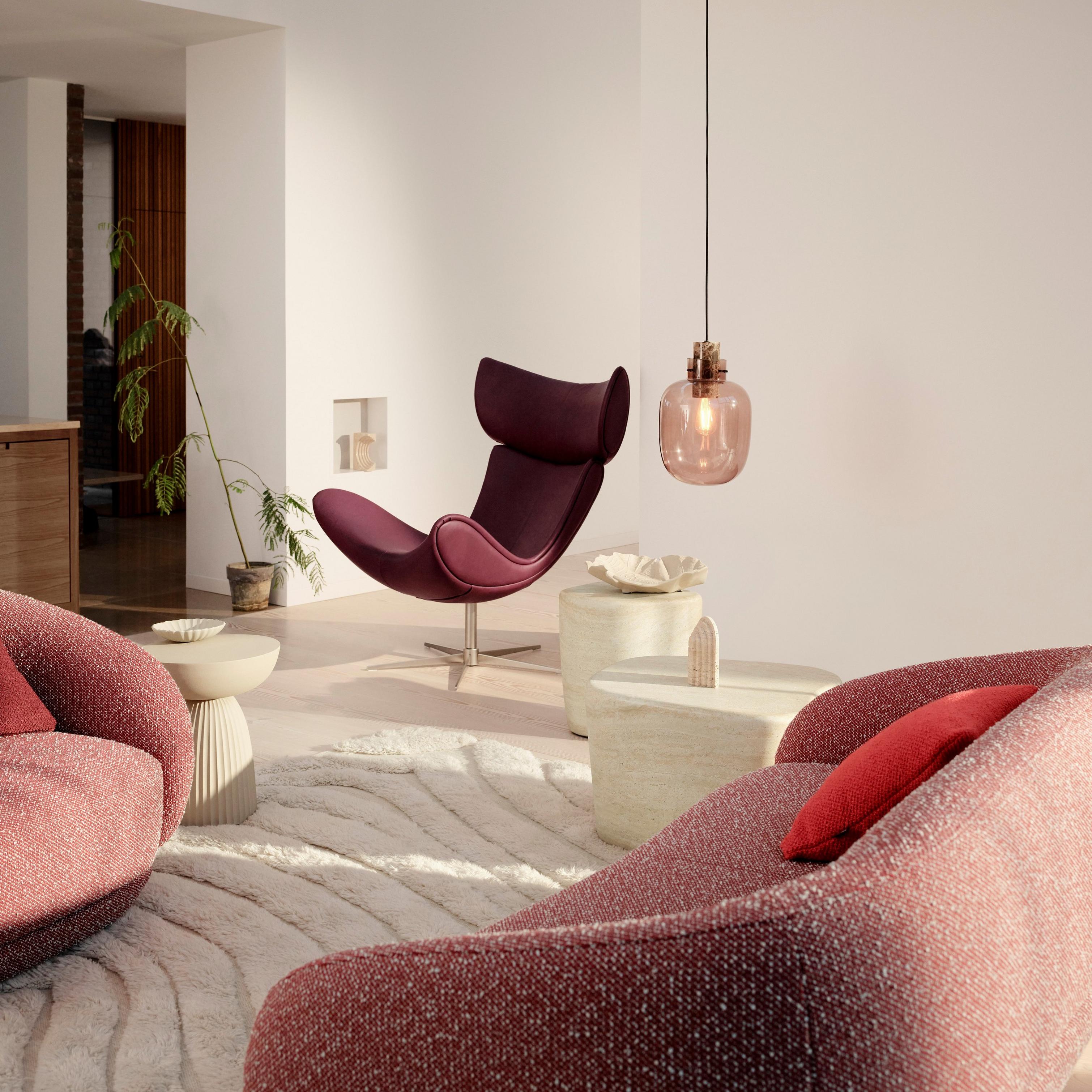 Stylish living room with a red Bolzano sofa and chair, a maroon lounge Imola chair, Stockholm pendant light, round tables, and potted plants.