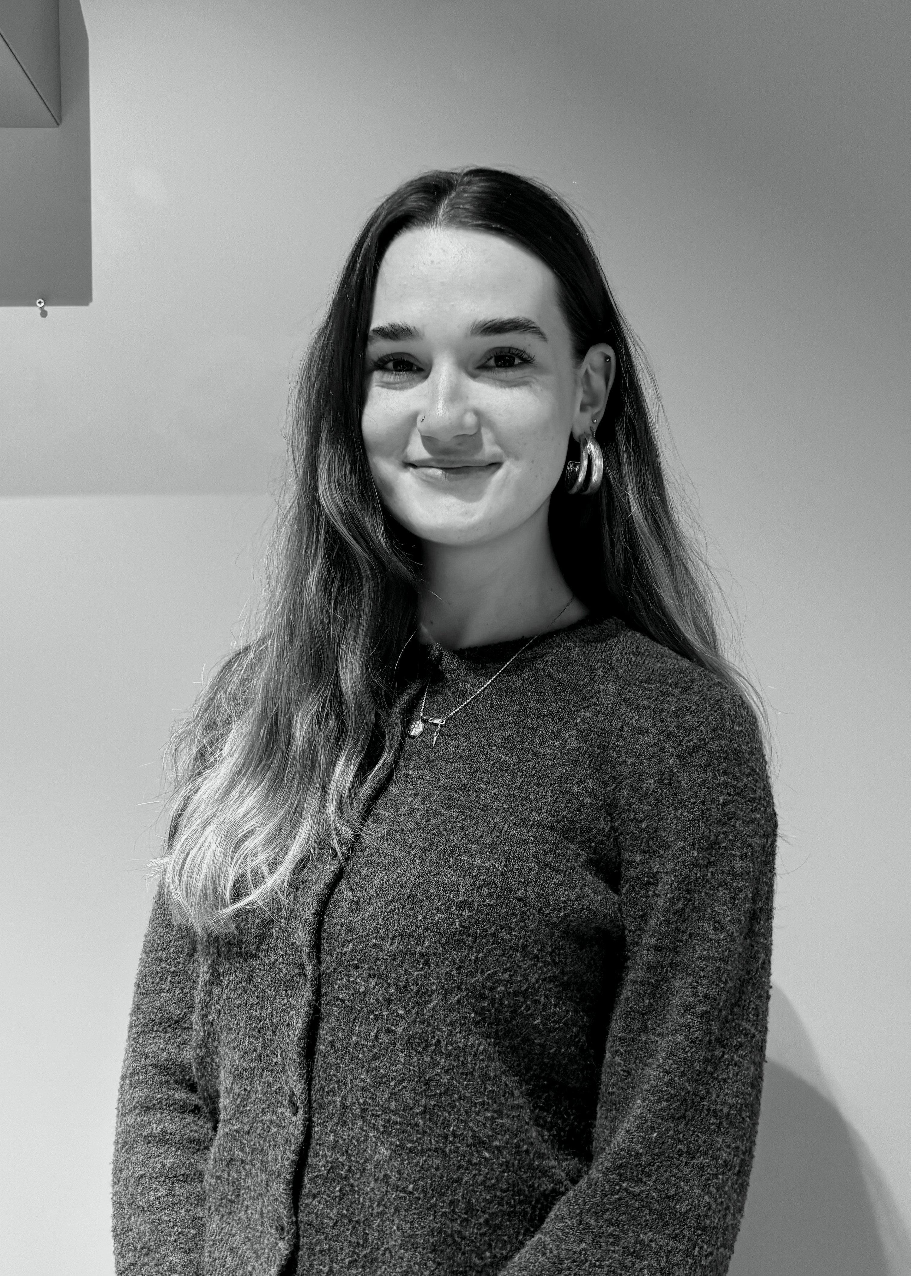 Woman wearing a knit jumper with hoop earrings and a necklace, smiling at the camera.