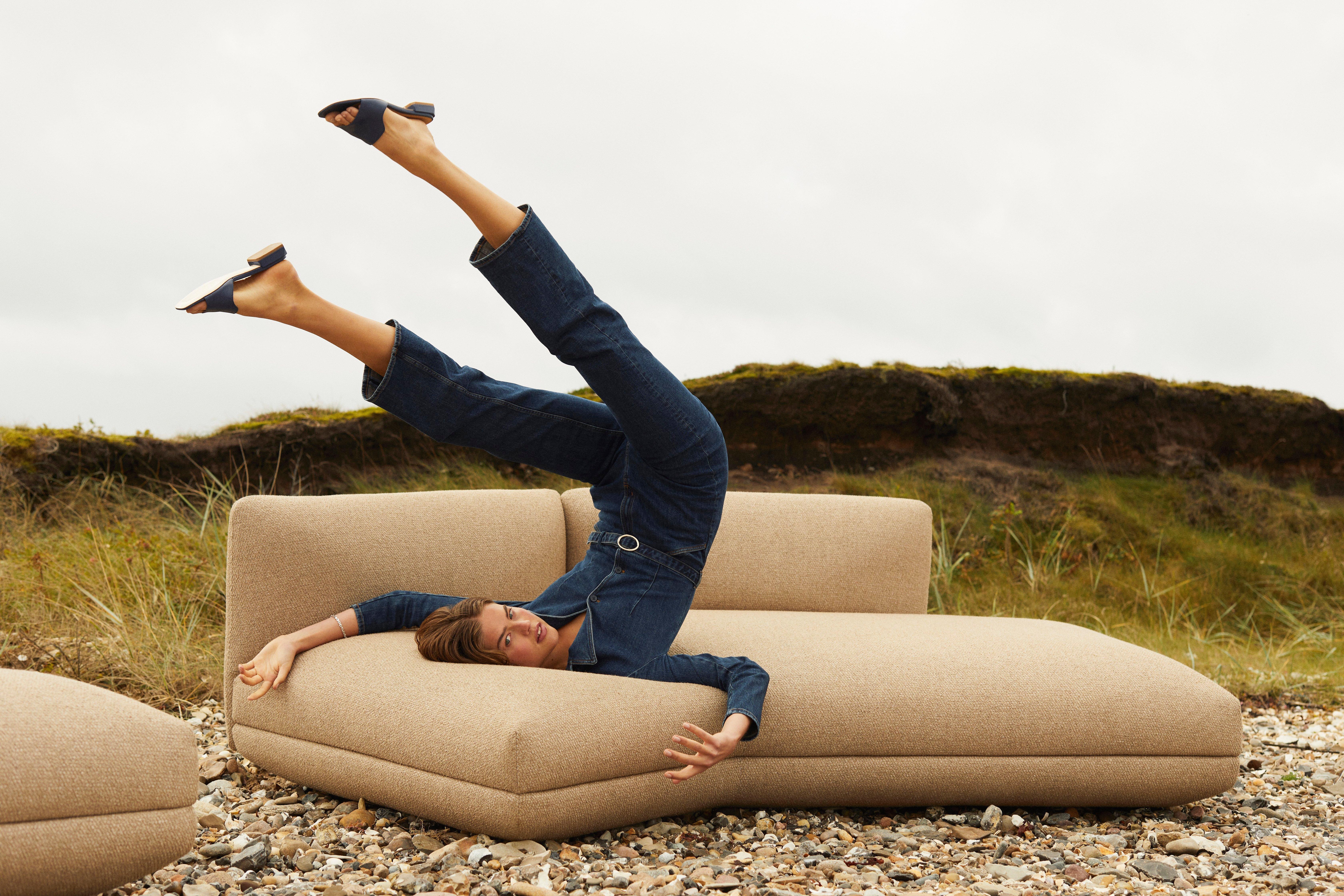 Mujer recostada sobre el sofá Salamanca tapizado en tela Lazio marrón en un ambiente de playa.