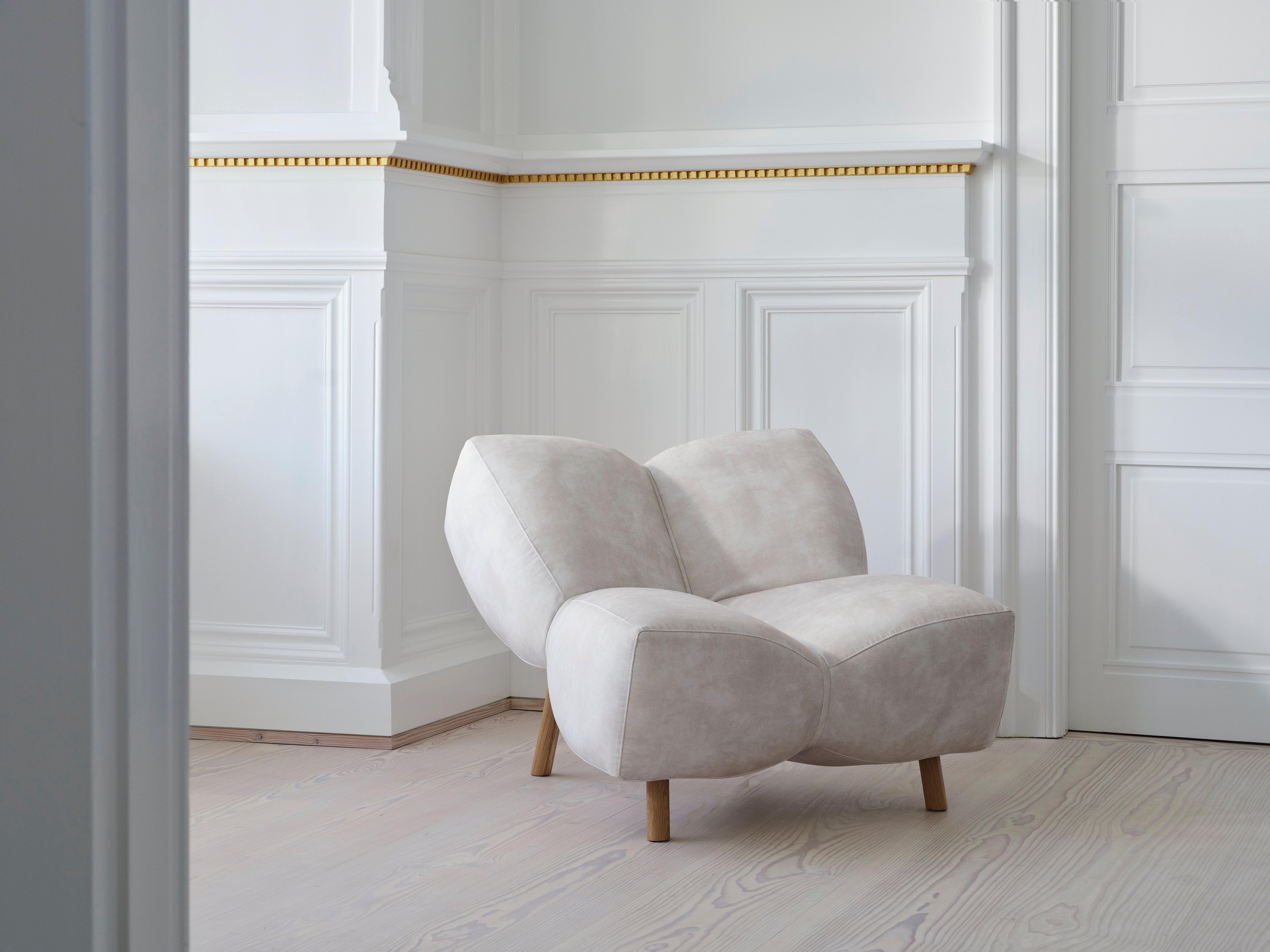Modern beige armchair with wooden legs in a white-panelled room.