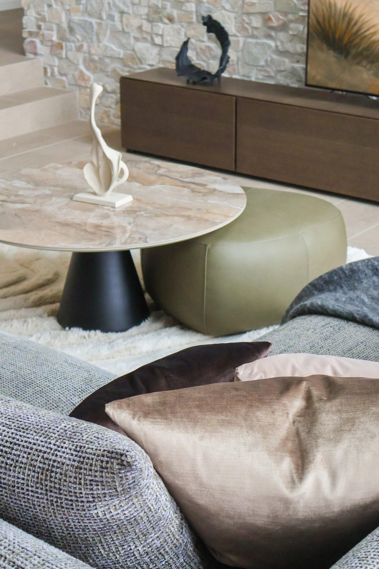 Bord med marmortopp, skulptur, grønn puff og grå sofa med puter i stue.