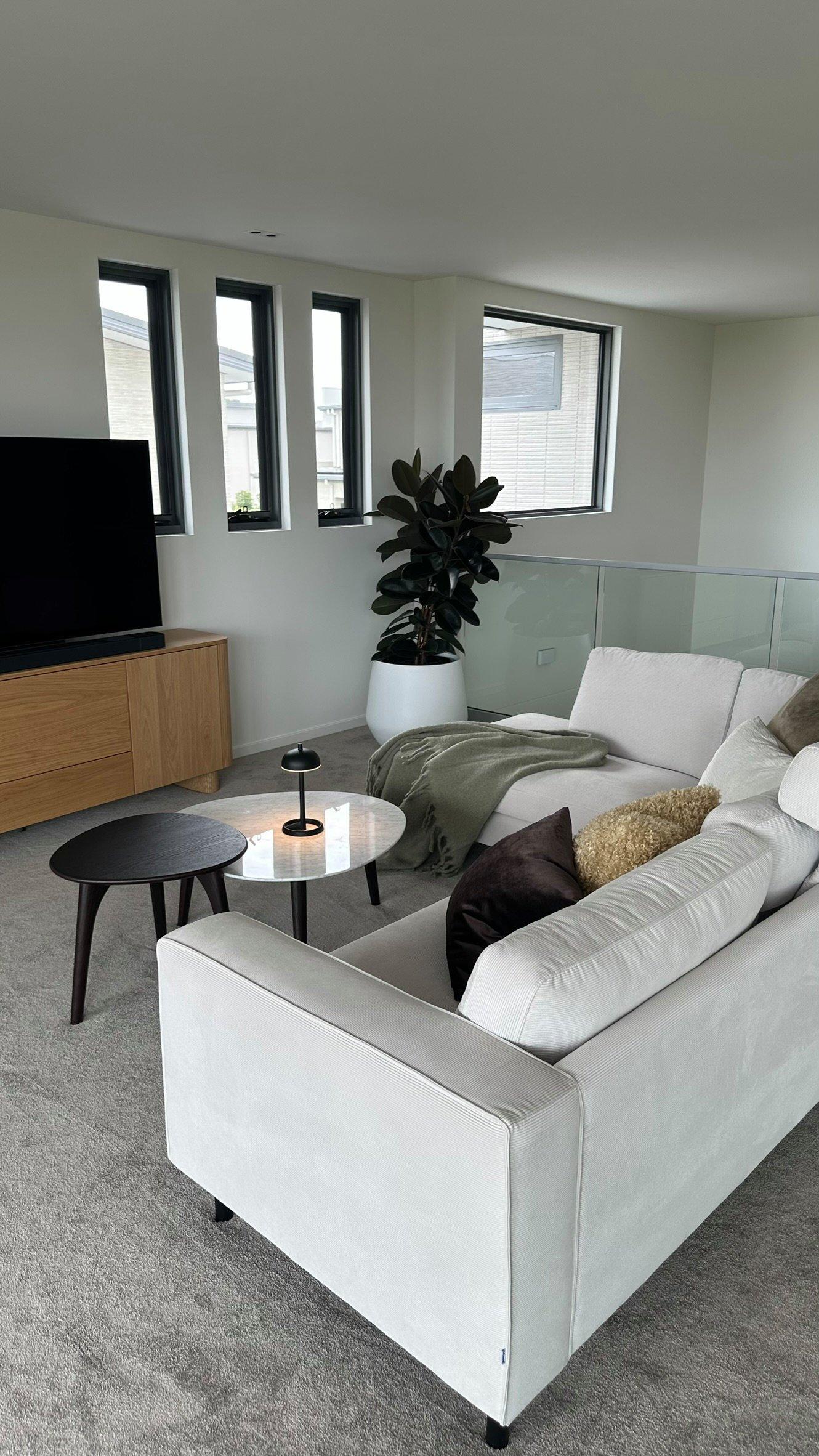 Moderne stue med hvit sofa, småbord, TV, og stor plante i hjørnet.