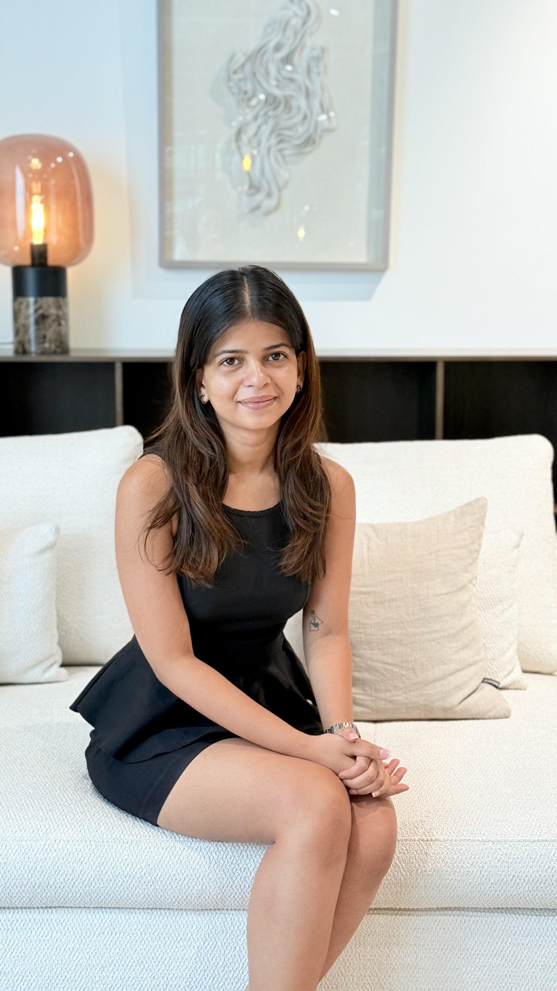 Woman sitting on a sofa wearing a sleeveless black dress.
